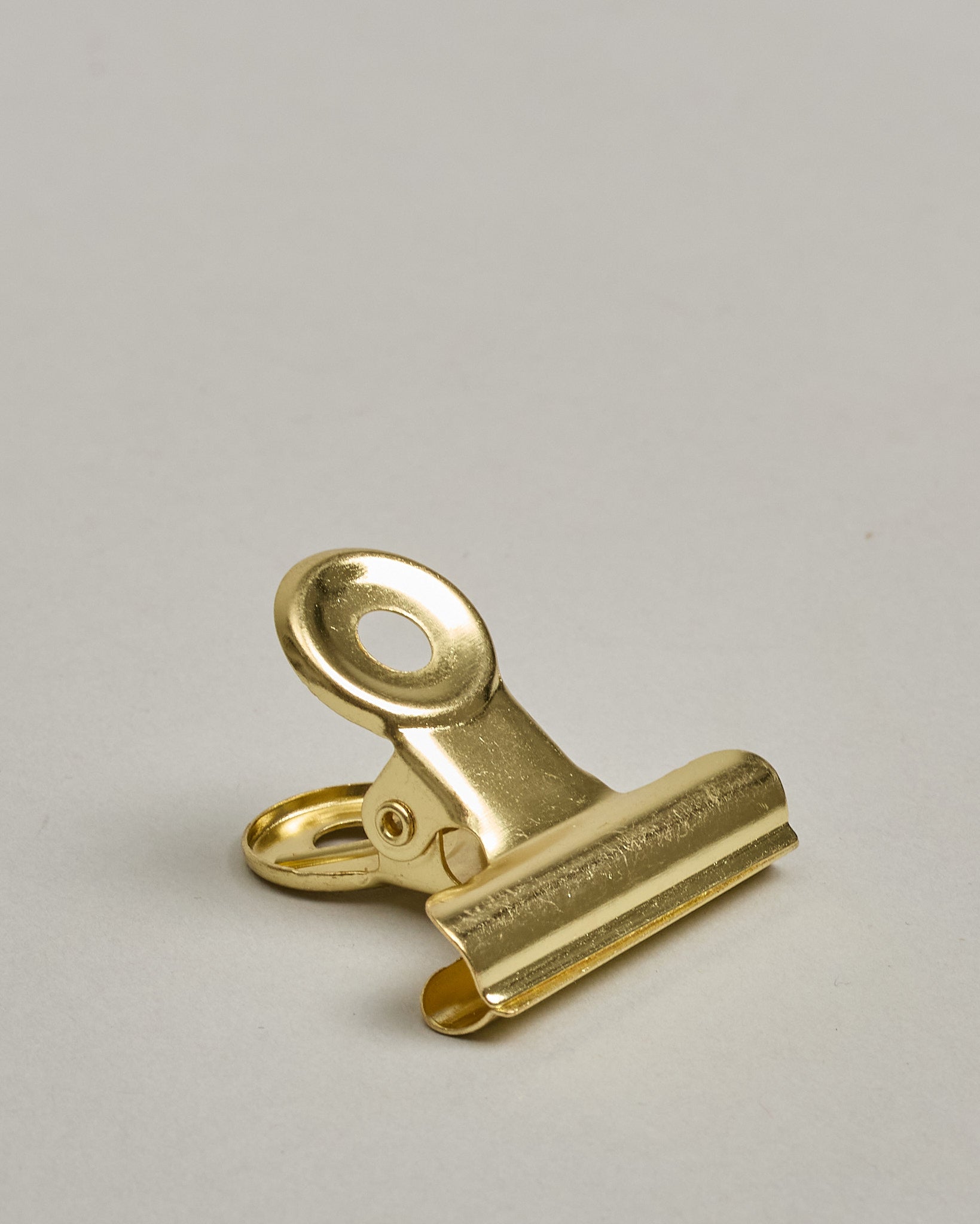 Ein einzelner Metall-Clip in gold mit einem Loch in den Greifarmen an denen man sie oben öffnen kann. #9