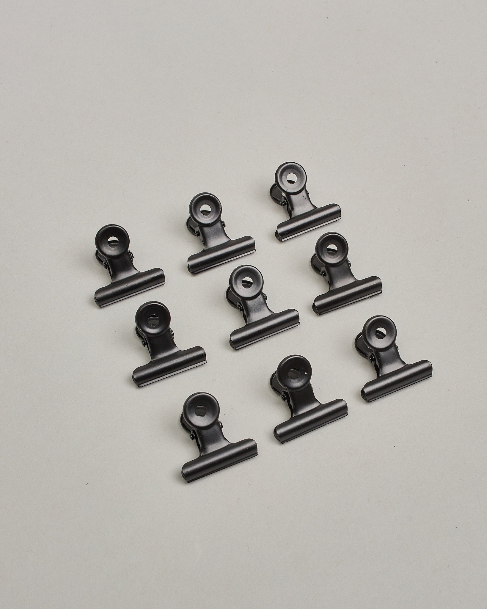 Ein zehnerset von Metall-Clips in mattem schwarz mit einem Loch in den Greifarmen an denen man sie oben öffnen kann. #15