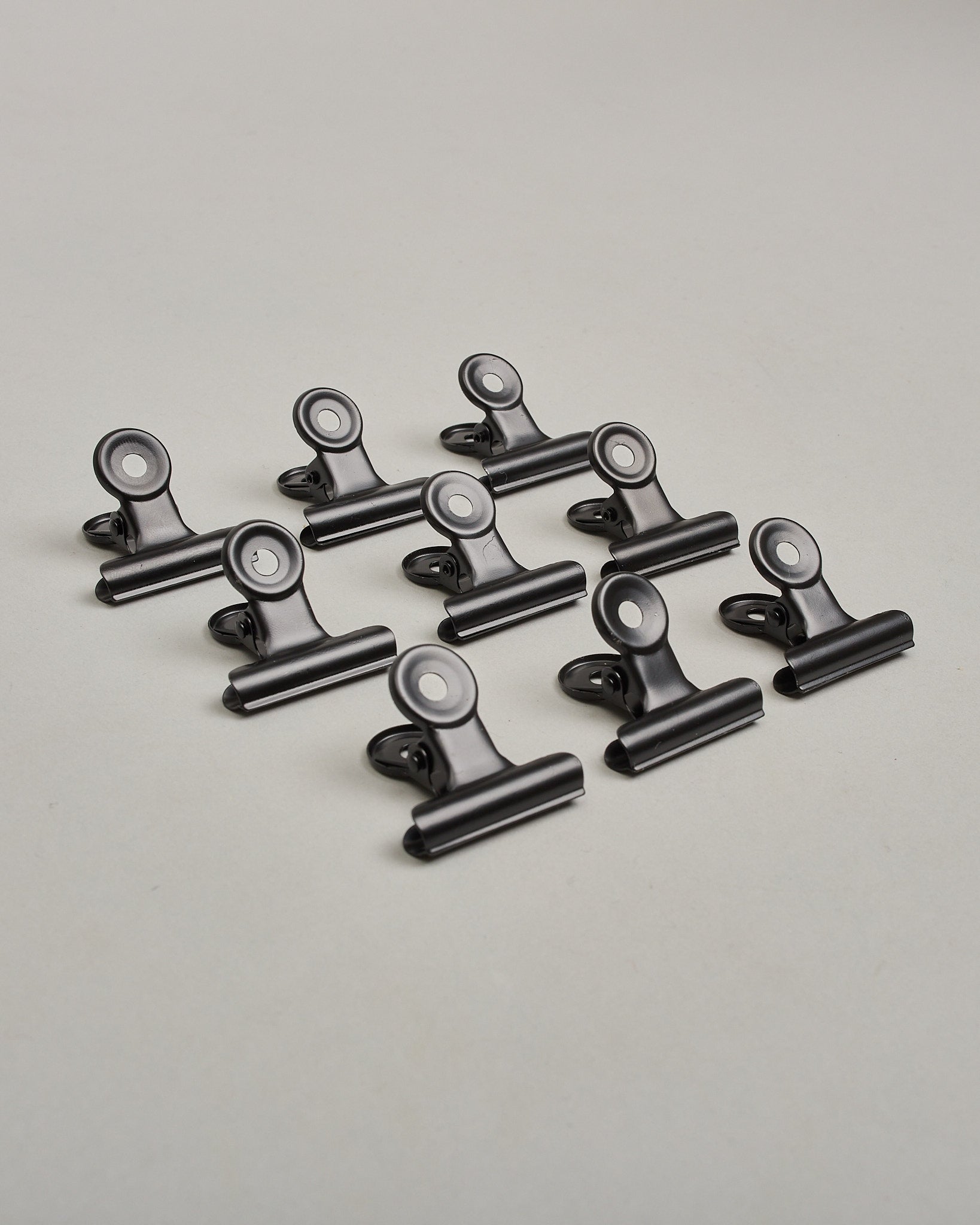 Ein zehnerset von Metall-Clips in mattem schwarz mit einem Loch in den Greifarmen an denen man sie oben öffnen kann. #14