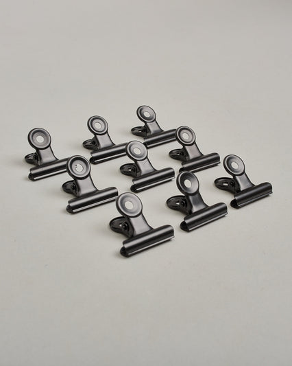 Ein zehnerset von Metall-Clips in mattem schwarz mit einem Loch in den Greifarmen an denen man sie oben öffnen kann. #14
