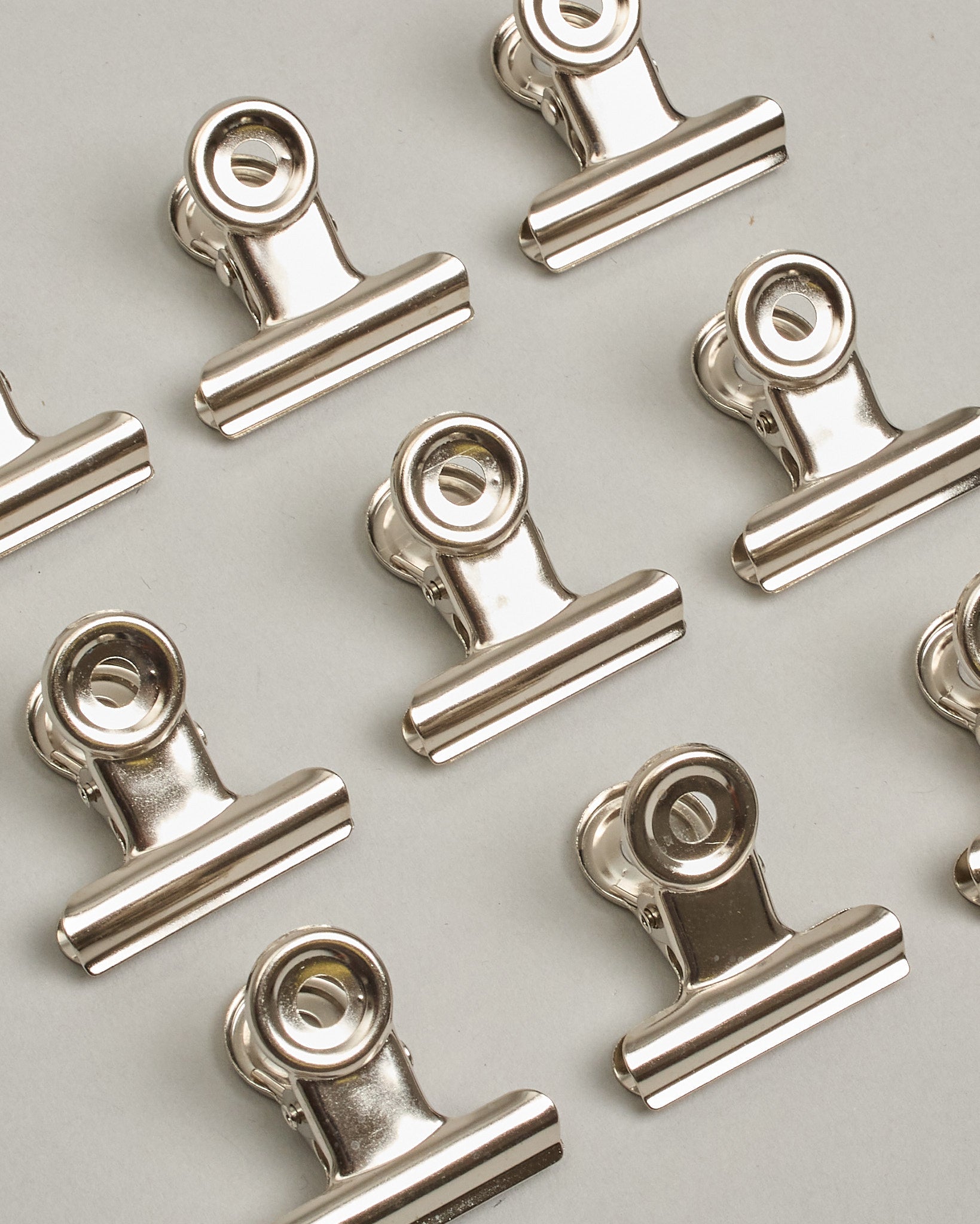 Ein einzelner Metall-Clip in silber mit einem Loch in den Greifarmen an denen man sie oben öffnen kann. #21