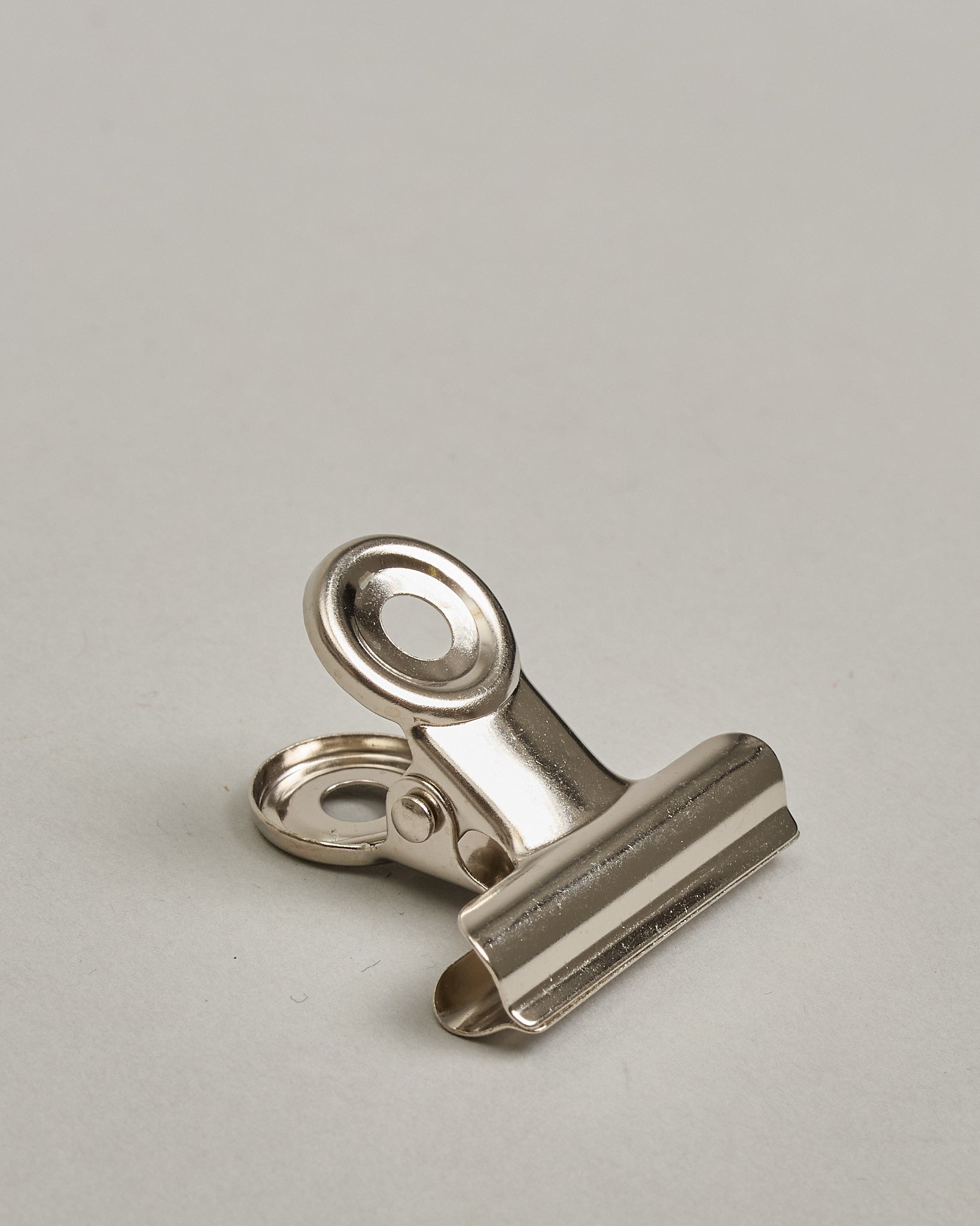 Ein einzelner Metall-Clip in silber mit einem Loch in den Greifarmen an denen man sie oben öffnen kann. #22