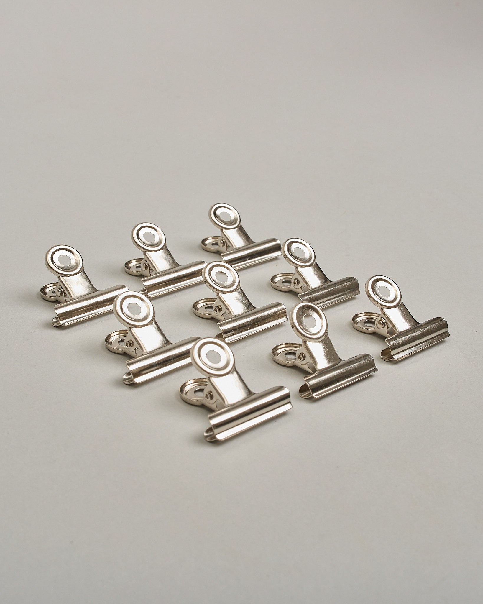 Ein einzelner Metall-Clip in silber mit einem Loch in den Greifarmen an denen man sie oben öffnen kann. #18