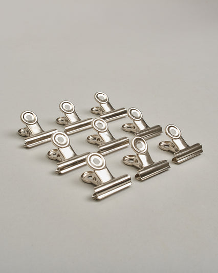 Ein einzelner Metall-Clip in silber mit einem Loch in den Greifarmen an denen man sie oben öffnen kann. #18