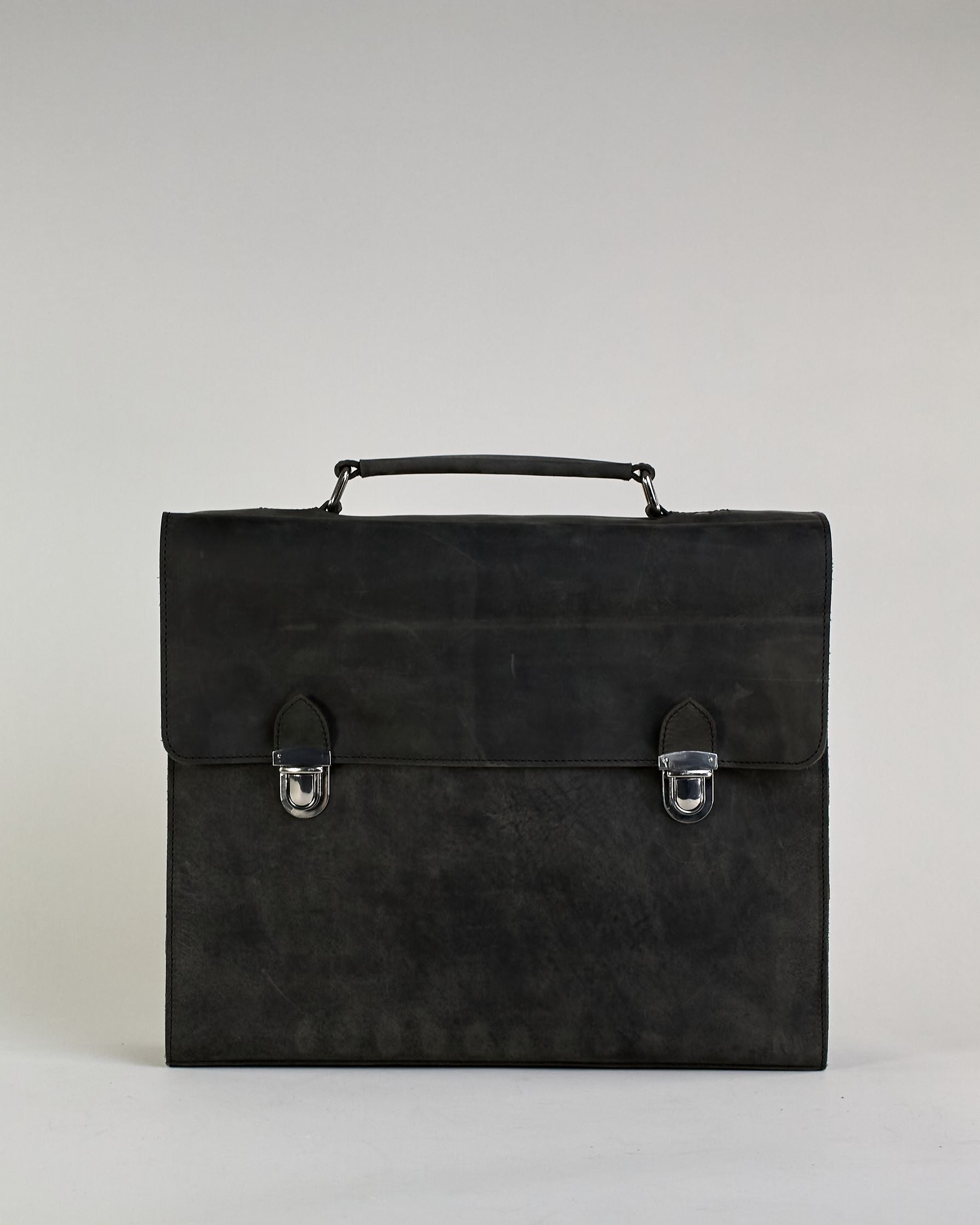 Schwarze Aktentasche aus Hunterleder mit Tragegriff, abnehmbarem Schulterriemen, Metallverschlüssen sowie Innenfächer. Das Lederist anfangs matt und entwickelt mit der Zeit eine individuelle Patina. Logo Prägung unter der Lasche mit zwei Metallverschlüssen in klassischem Schultaschen-Stil. #37