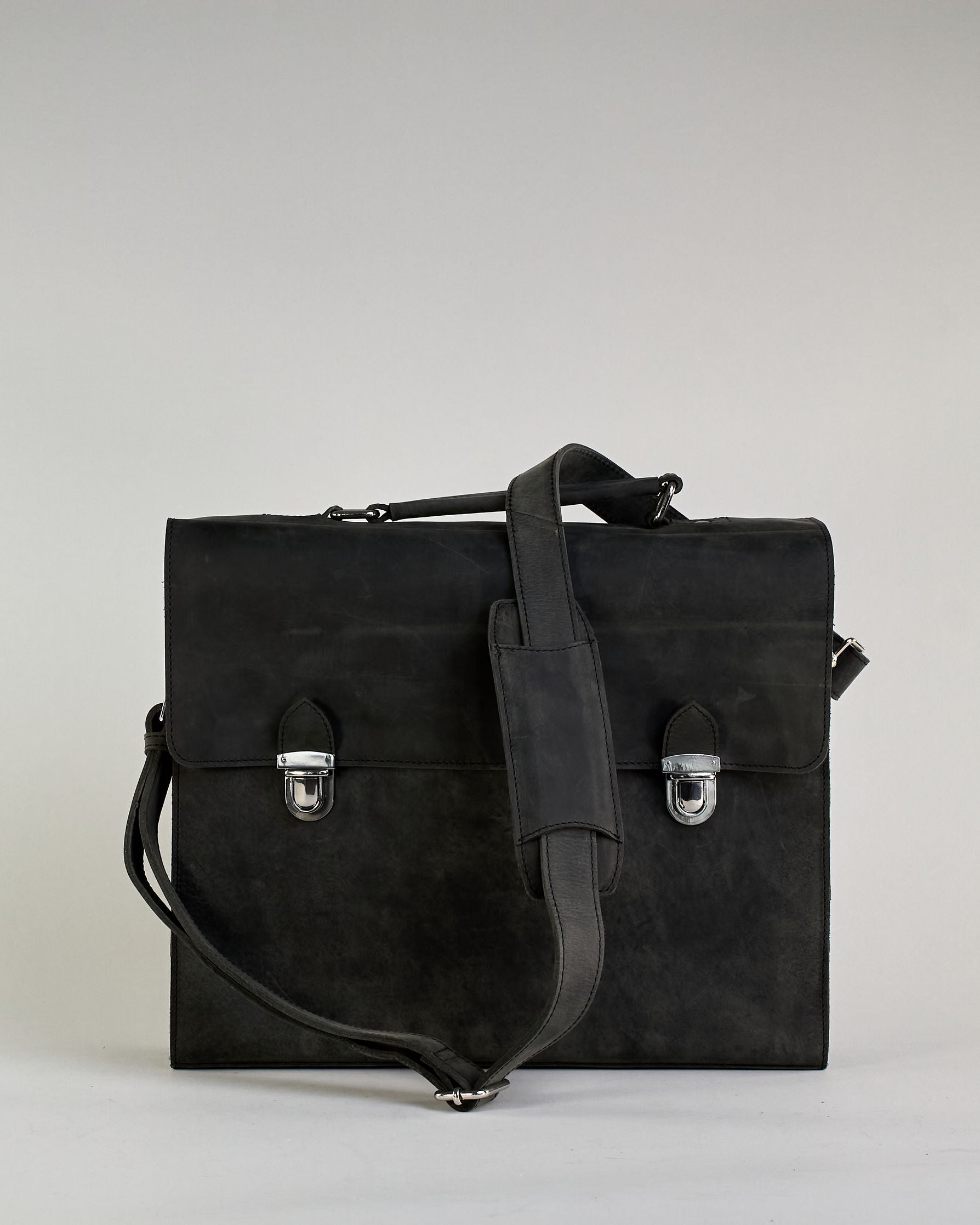 Schwarze Aktentasche aus Hunterleder mit Tragegriff, abnehmbarem Schulterriemen, Metallverschlüssen sowie Innenfächer. Das Lederist anfangs matt und entwickelt mit der Zeit eine individuelle Patina. Logo Prägung unter der Lasche mit zwei Metallverschlüssen in klassischem Schultaschen-Stil. #38