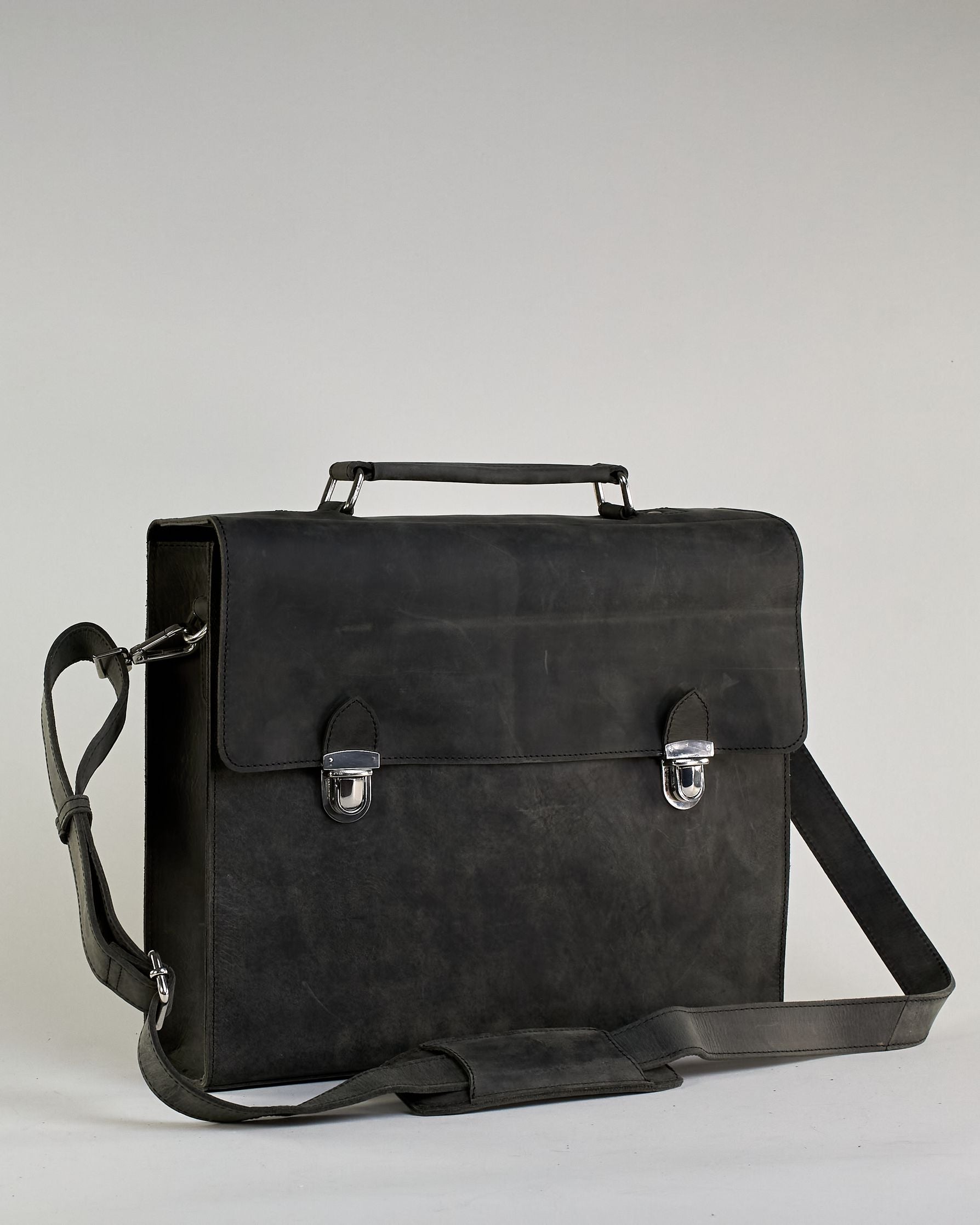 Schwarze Aktentasche aus Hunterleder mit Tragegriff, abnehmbarem Schulterriemen, Metallverschlüssen sowie Innenfächer. Das Lederist anfangs matt und entwickelt mit der Zeit eine individuelle Patina. Logo Prägung unter der Lasche mit zwei Metallverschlüssen in klassischem Schultaschen-Stil. #39