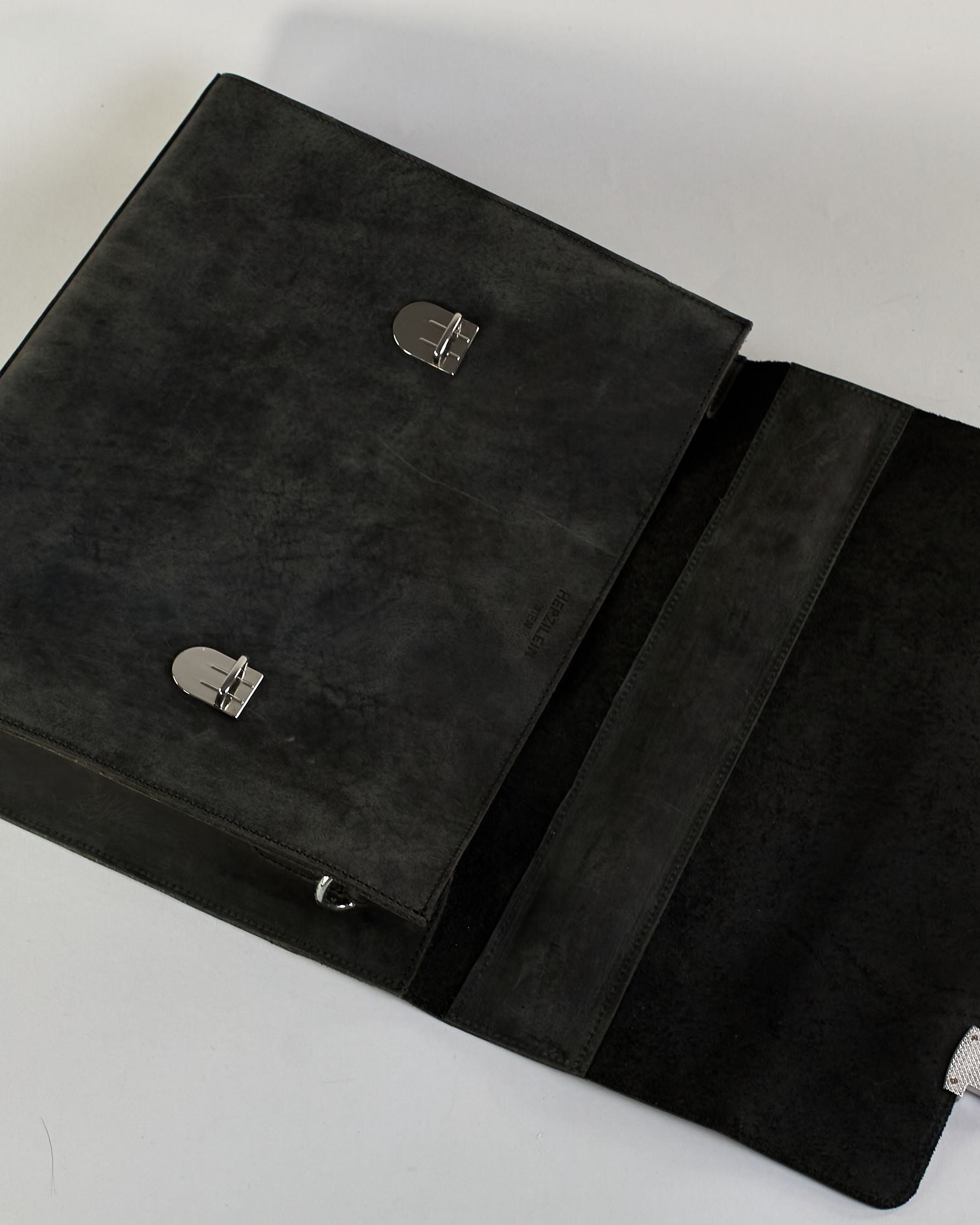 Schwarze Aktentasche aus Hunterleder mit Tragegriff, abnehmbarem Schulterriemen, Metallverschlüssen sowie Innenfächer. Das Lederist anfangs matt und entwickelt mit der Zeit eine individuelle Patina. Logo Prägung unter der Lasche mit zwei Metallverschlüssen in klassischem Schultaschen-Stil. #40