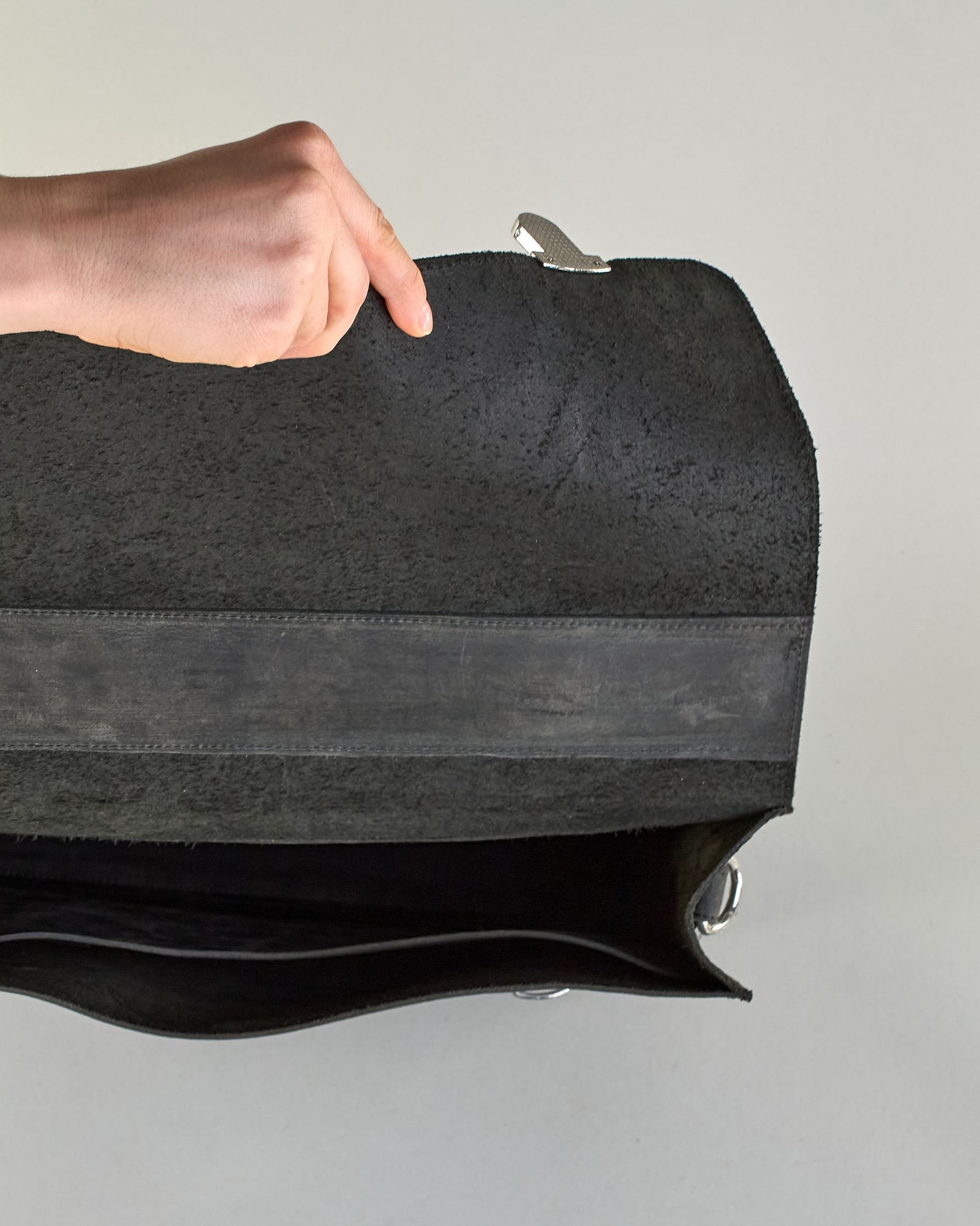 Schwarze Aktentasche aus Hunterleder mit Tragegriff, abnehmbarem Schulterriemen, Metallverschlüssen sowie Innenfächer. Das Lederist anfangs matt und entwickelt mit der Zeit eine individuelle Patina. Logo Prägung unter der Lasche mit zwei Metallverschlüssen in klassischem Schultaschen-Stil. #41