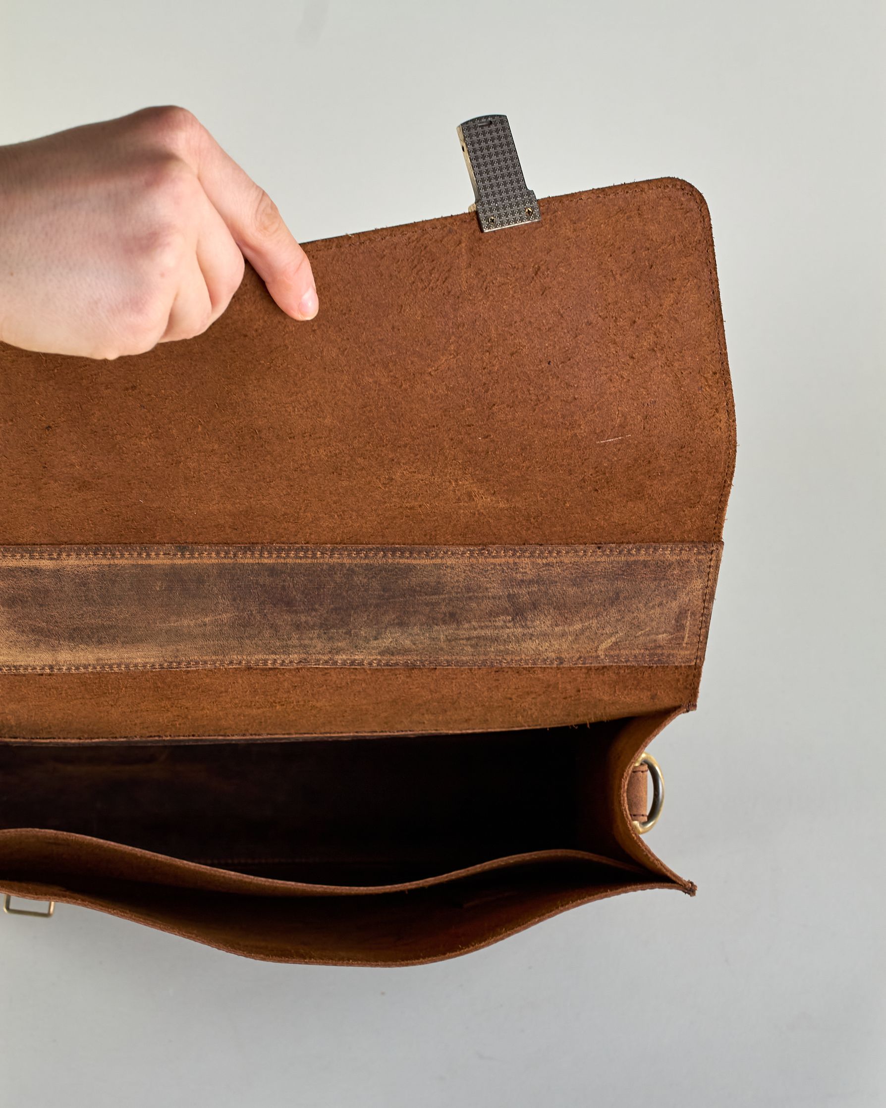 Schwarze Aktentasche aus Hunterleder mit Tragegriff, abnehmbarem Schulterriemen, Metallverschlüssen sowie Innenfächer. Das Lederist anfangs matt und entwickelt mit der Zeit eine individuelle Patina. Logo Prägung unter der Lasche mit zwei Metallverschlüssen in klassischem Schultaschen-Stil. #45