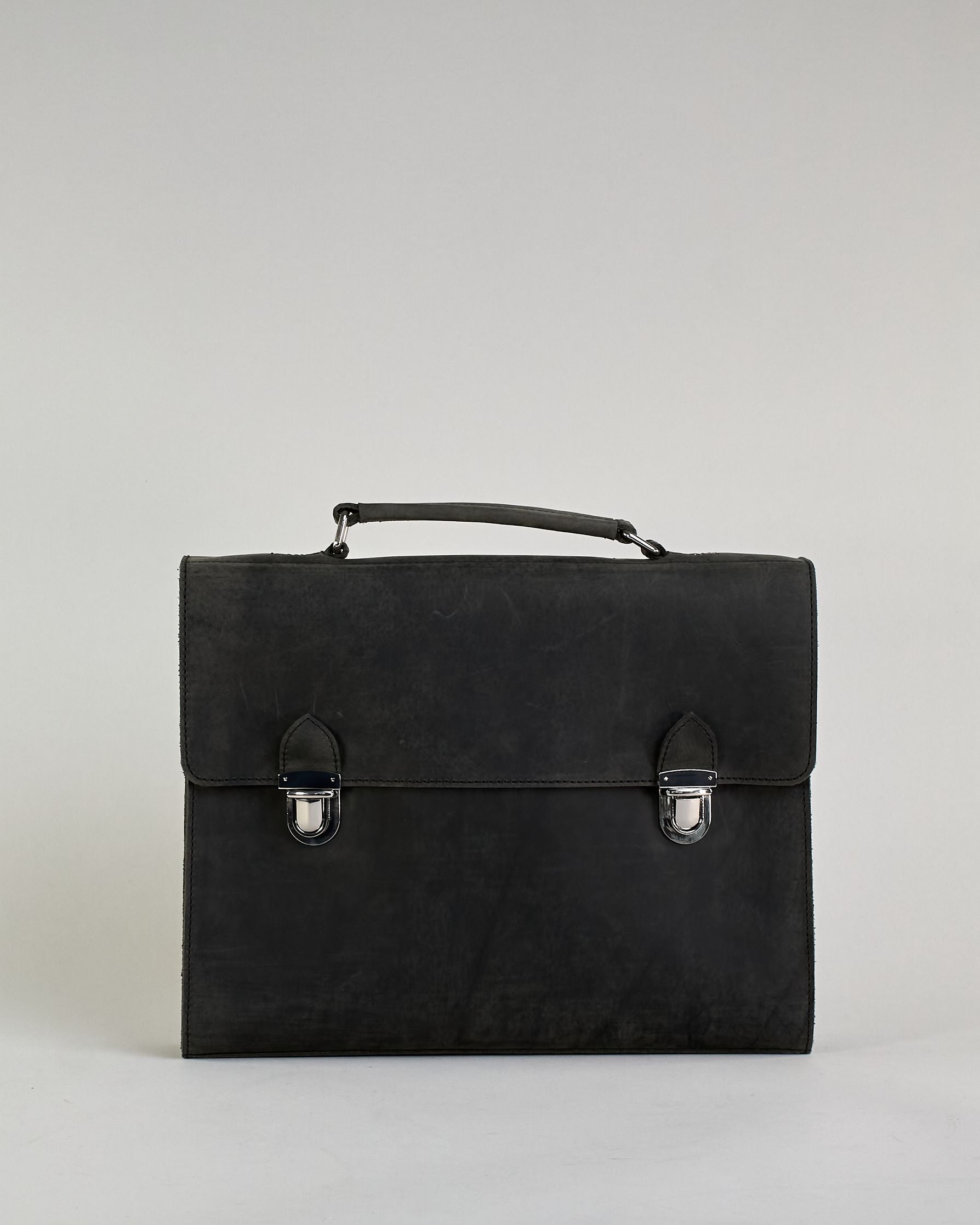 Schwarze Aktentasche aus Hunterleder mit Tragegriff, abnehmbarem Schulterriemen, Metallverschlüssen sowie Innenfächer. Das Lederist anfangs matt und entwickelt mit der Zeit eine individuelle Patina. Logo Prägung unter der Lasche mit zwei Metallverschlüssen in klassischem Schultaschen-Stil. #1