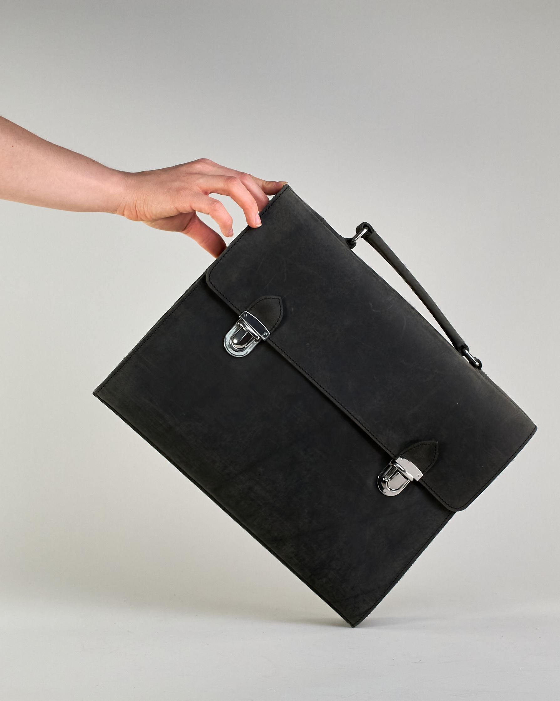Schwarze Aktentasche aus Hunterleder mit Tragegriff, abnehmbarem Schulterriemen, Metallverschlüssen sowie Innenfächer. Das Lederist anfangs matt und entwickelt mit der Zeit eine individuelle Patina. Logo Prägung unter der Lasche mit zwei Metallverschlüssen in klassischem Schultaschen-Stil. #2