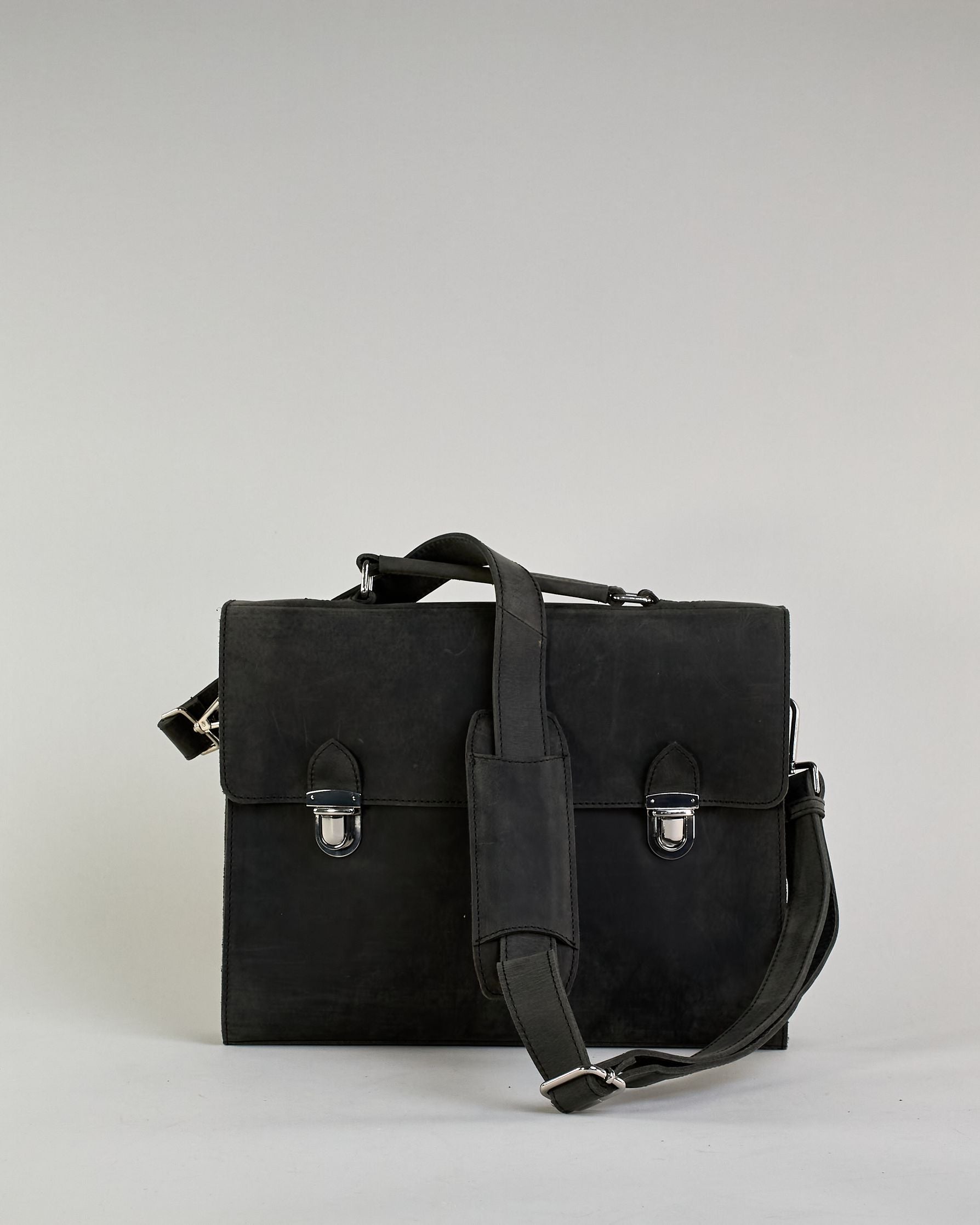 Schwarze Aktentasche aus Hunterleder mit Tragegriff, abnehmbarem Schulterriemen, Metallverschlüssen sowie Innenfächer. Das Lederist anfangs matt und entwickelt mit der Zeit eine individuelle Patina. Logo Prägung unter der Lasche mit zwei Metallverschlüssen in klassischem Schultaschen-Stil. #6