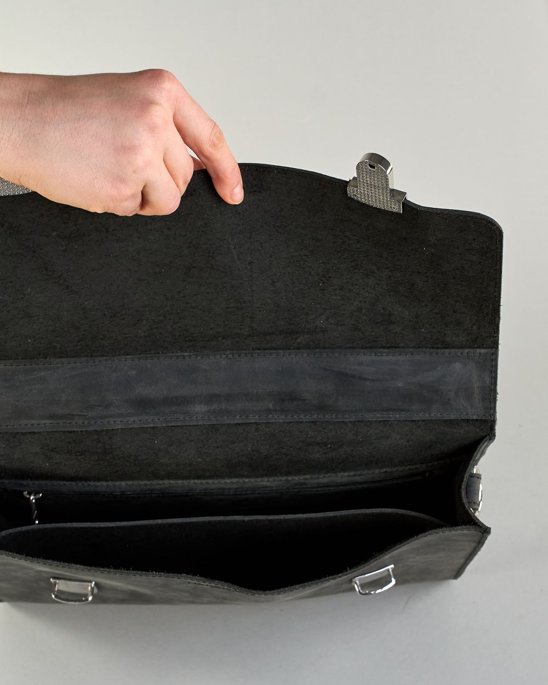 Schwarze Aktentasche aus Hunterleder mit Tragegriff, abnehmbarem Schulterriemen, Metallverschlüssen sowie Innenfächer. Das Lederist anfangs matt und entwickelt mit der Zeit eine individuelle Patina. Logo Prägung unter der Lasche mit zwei Metallverschlüssen in klassischem Schultaschen-Stil. #7