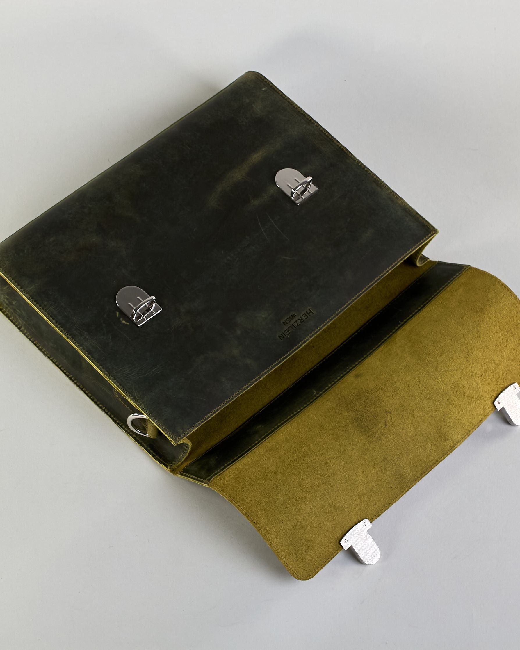 Schwarze Aktentasche aus Hunterleder mit Tragegriff, abnehmbarem Schulterriemen, Metallverschlüssen sowie Innenfächer. Das Lederist anfangs matt und entwickelt mit der Zeit eine individuelle Patina. Logo Prägung unter der Lasche mit zwei Metallverschlüssen in klassischem Schultaschen-Stil. #16