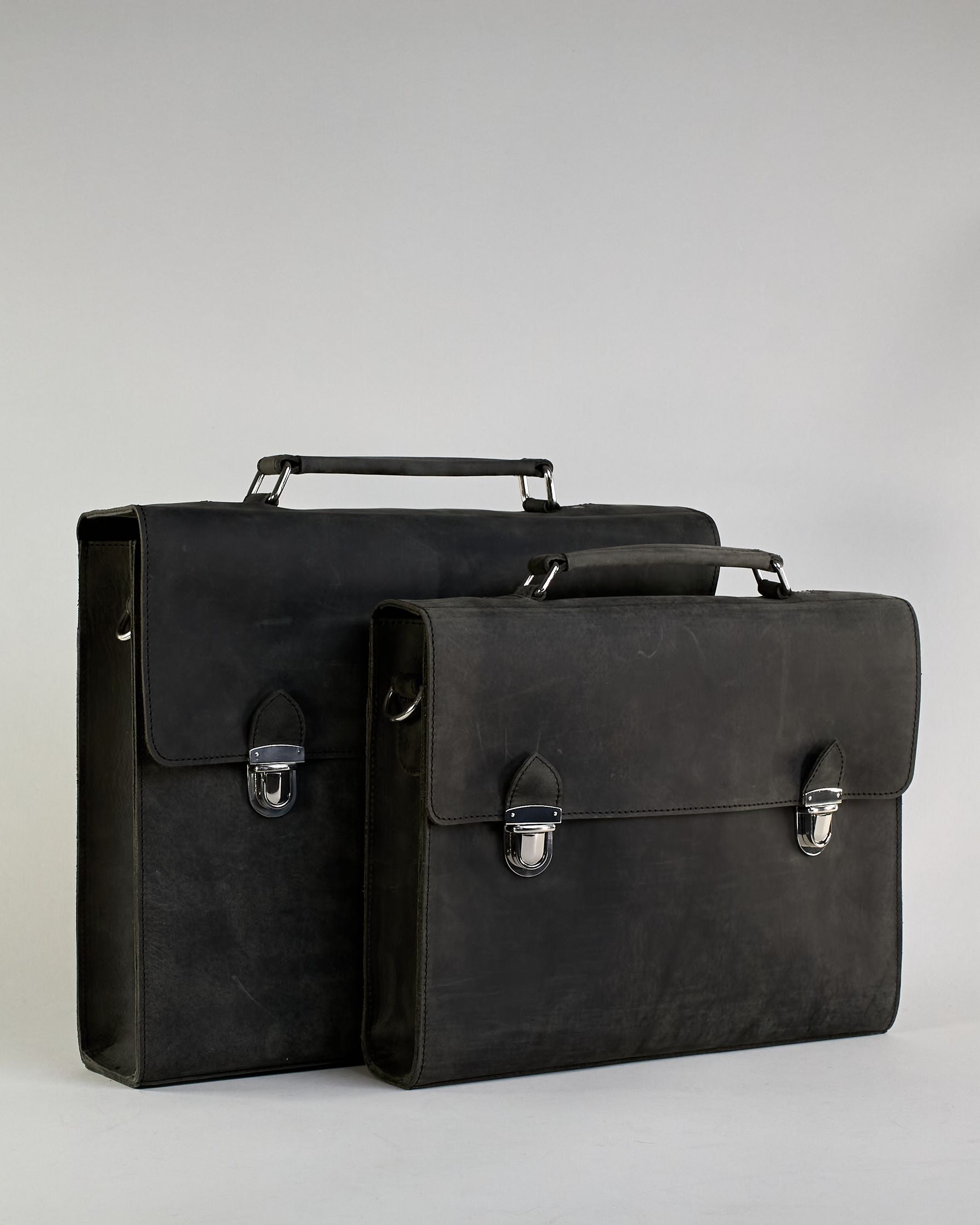 Schwarze Aktentasche aus Hunterleder mit Tragegriff, abnehmbarem Schulterriemen, Metallverschlüssen sowie Innenfächer. Das Lederist anfangs matt und entwickelt mit der Zeit eine individuelle Patina. Logo Prägung unter der Lasche mit zwei Metallverschlüssen in klassischem Schultaschen-Stil. #17