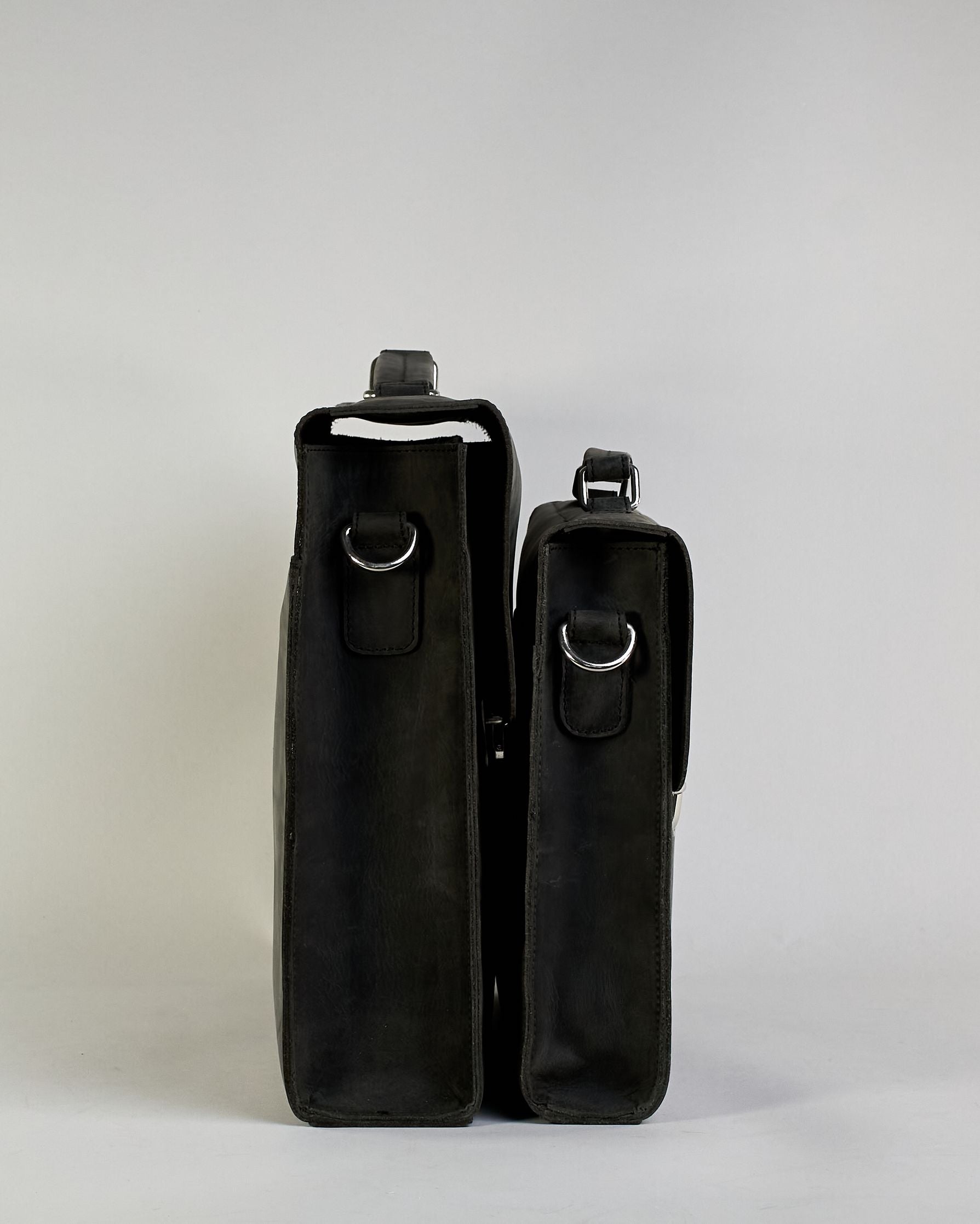 Schwarze Aktentasche aus Hunterleder mit Tragegriff, abnehmbarem Schulterriemen, Metallverschlüssen sowie Innenfächer. Das Lederist anfangs matt und entwickelt mit der Zeit eine individuelle Patina. Logo Prägung unter der Lasche mit zwei Metallverschlüssen in klassischem Schultaschen-Stil. #21