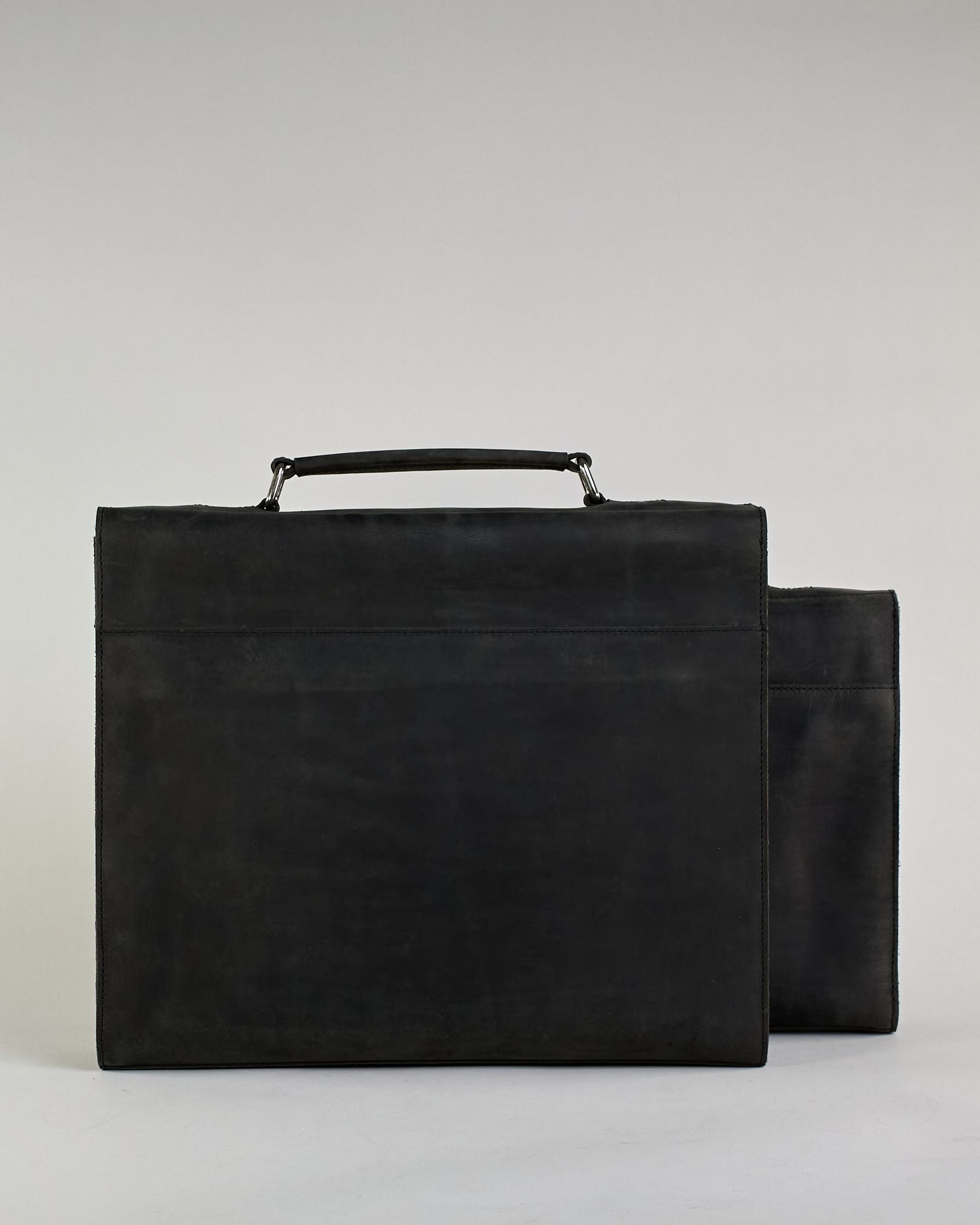 Schwarze Aktentasche aus Hunterleder mit Tragegriff, abnehmbarem Schulterriemen, Metallverschlüssen sowie Innenfächer. Das Lederist anfangs matt und entwickelt mit der Zeit eine individuelle Patina. Logo Prägung unter der Lasche mit zwei Metallverschlüssen in klassischem Schultaschen-Stil. #22