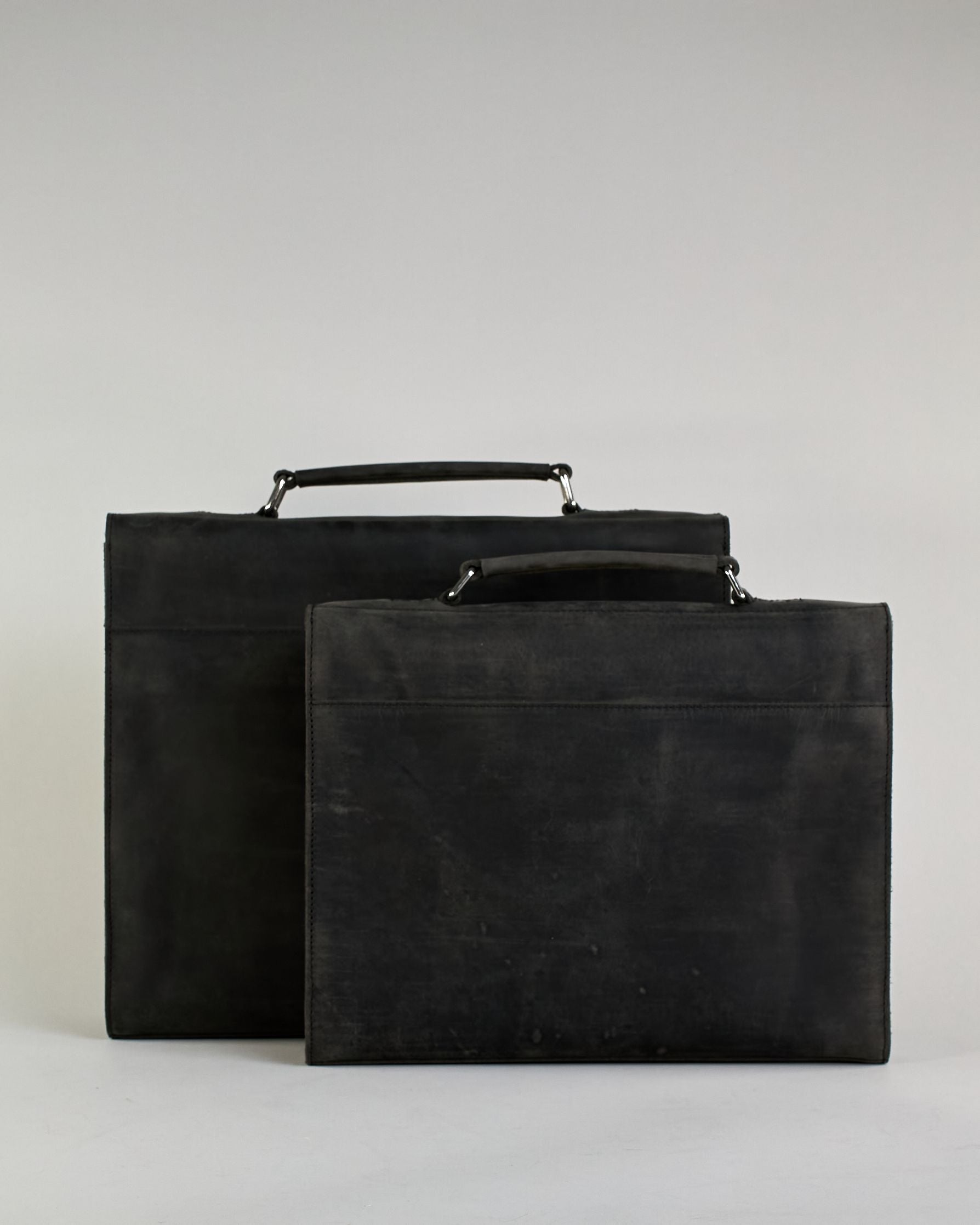 Schwarze Aktentasche aus Hunterleder mit Tragegriff, abnehmbarem Schulterriemen, Metallverschlüssen sowie Innenfächer. Das Lederist anfangs matt und entwickelt mit der Zeit eine individuelle Patina. Logo Prägung unter der Lasche mit zwei Metallverschlüssen in klassischem Schultaschen-Stil. #23