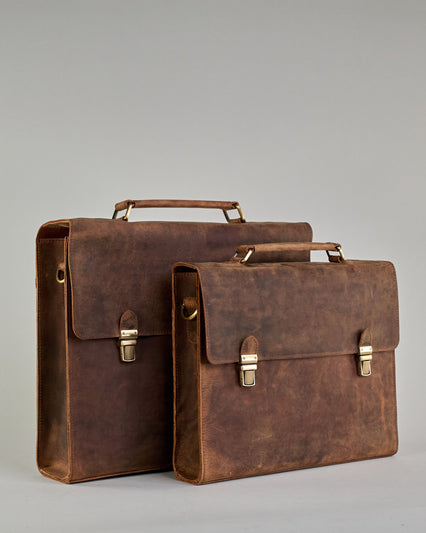 Schwarze Aktentasche aus Hunterleder mit Tragegriff, abnehmbarem Schulterriemen, Metallverschlüssen sowie Innenfächer. Das Lederist anfangs matt und entwickelt mit der Zeit eine individuelle Patina. Logo Prägung unter der Lasche mit zwei Metallverschlüssen in klassischem Schultaschen-Stil. #28