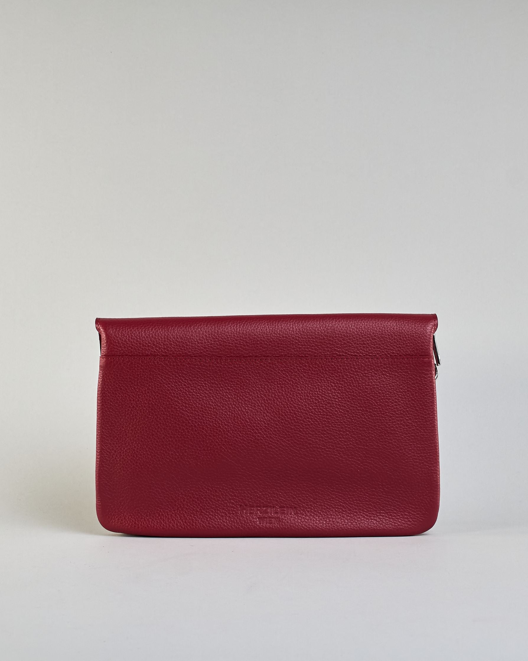 Einfärbige kleine Crossbody-Tasche aus genarbtem Rindleder mit Umschlaglasche und silbernem Druckknopf. Die Tasche enthält innen ein Zippfach, ein offenes Fach sowie ein schmales Zwischenfach. Auf der Rückseite ist eine Logoprägung "Herzilein-Wien" #3