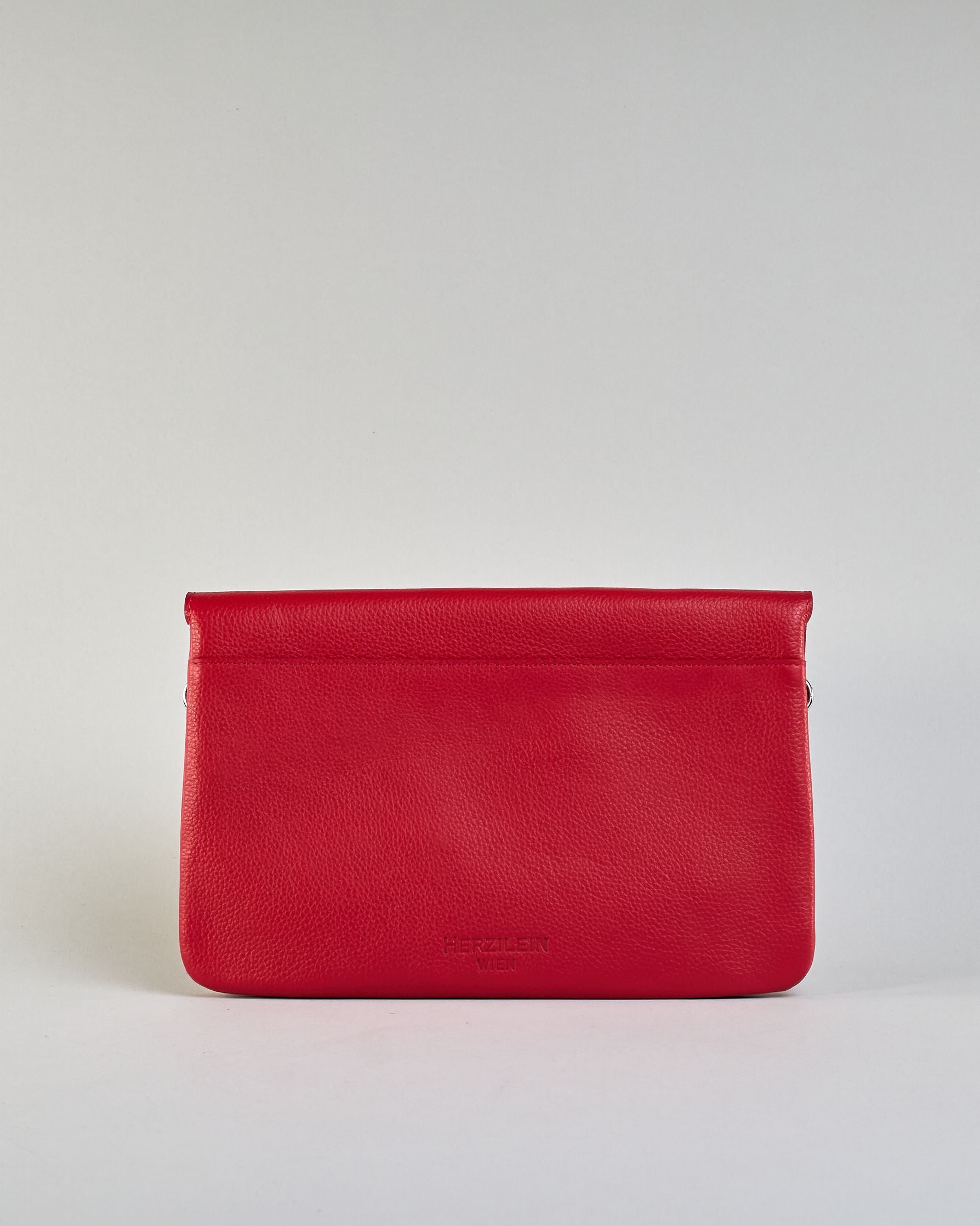 Einfärbige kleine Crossbody-Tasche aus genarbtem Rindleder mit Umschlaglasche und silbernem Druckknopf. Die Tasche enthält innen ein Zippfach, ein offenes Fach sowie ein schmales Zwischenfach. Auf der Rückseite ist eine Logoprägung "Herzilein-Wien" #15