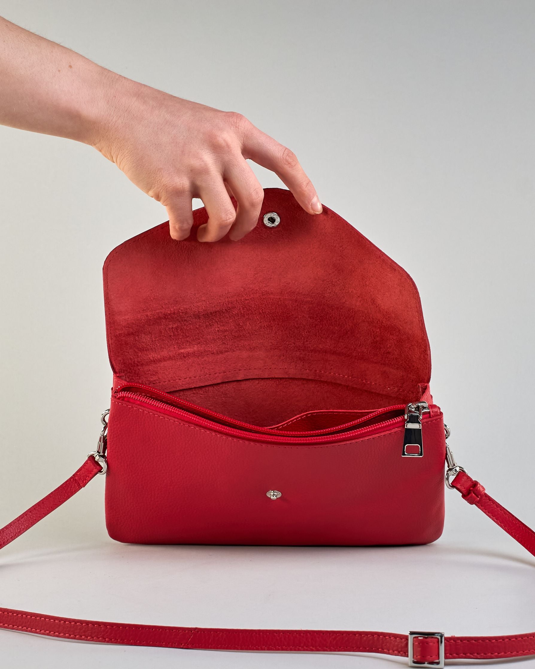 Einfärbige kleine Crossbody-Tasche aus genarbtem Rindleder mit Umschlaglasche und silbernem Druckknopf. Die Tasche enthält innen ein Zippfach, ein offenes Fach sowie ein schmales Zwischenfach. Auf der Rückseite ist eine Logoprägung "Herzilein-Wien" #18