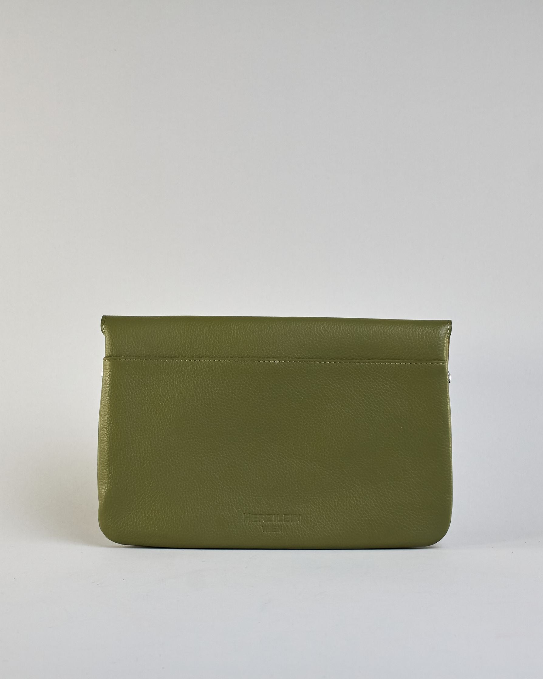 Einfärbige kleine Crossbody-Tasche aus genarbtem Rindleder mit Umschlaglasche und silbernem Druckknopf. Die Tasche enthält innen ein Zippfach, ein offenes Fach sowie ein schmales Zwischenfach. Auf der Rückseite ist eine Logoprägung "Herzilein-Wien" #21