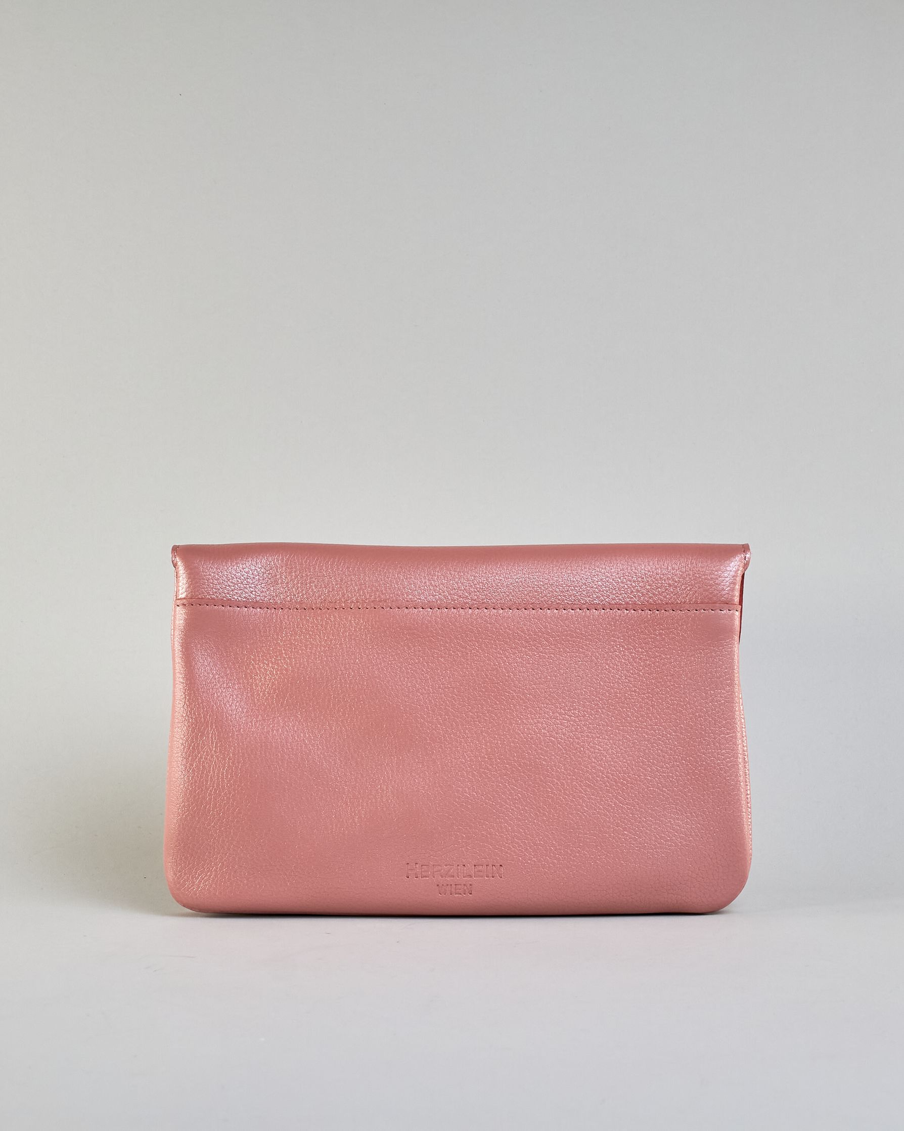 Einfärbige kleine Crossbody-Tasche aus genarbtem Rindleder mit Umschlaglasche und silbernem Druckknopf. Die Tasche enthält innen ein Zippfach, ein offenes Fach sowie ein schmales Zwischenfach. Auf der Rückseite ist eine Logoprägung "Herzilein-Wien" #26