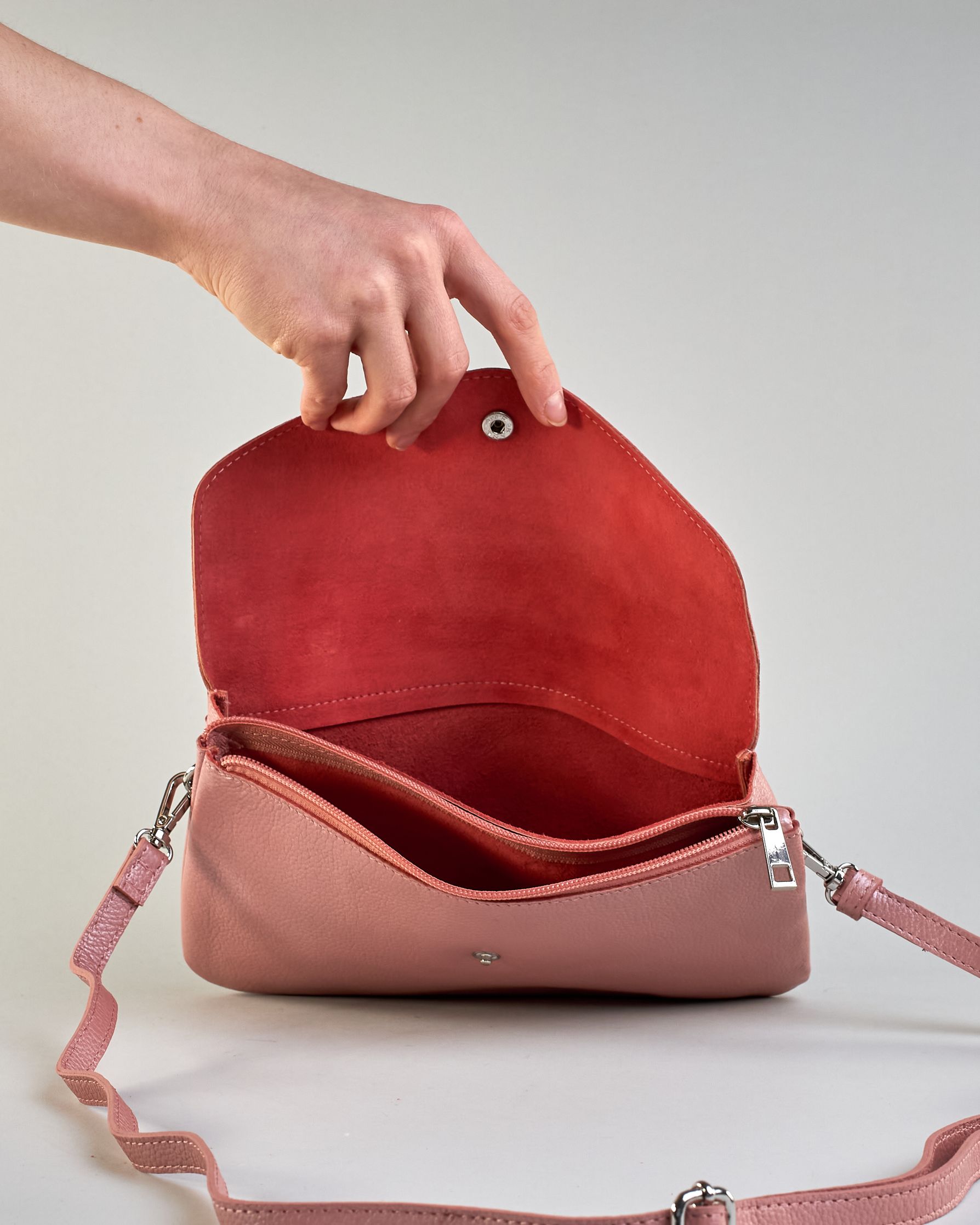 Einfärbige kleine Crossbody-Tasche aus genarbtem Rindleder mit Umschlaglasche und silbernem Druckknopf. Die Tasche enthält innen ein Zippfach, ein offenes Fach sowie ein schmales Zwischenfach. Auf der Rückseite ist eine Logoprägung "Herzilein-Wien" #29