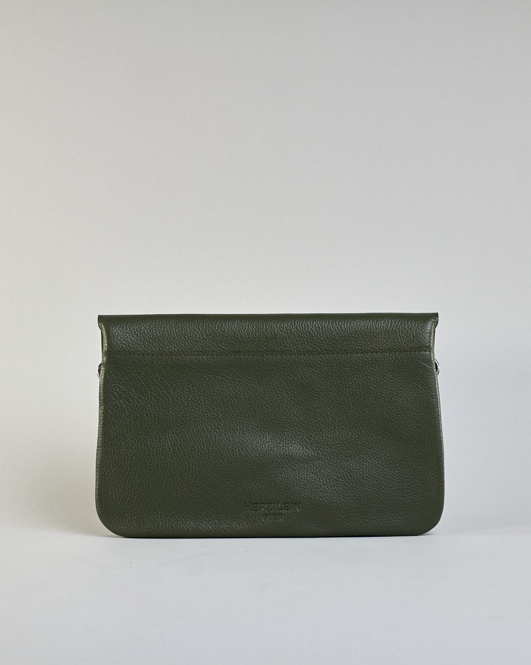 Einfärbige kleine Crossbody-Tasche aus genarbtem Rindleder mit Umschlaglasche und silbernem Druckknopf. Die Tasche enthält innen ein Zippfach, ein offenes Fach sowie ein schmales Zwischenfach. Auf der Rückseite ist eine Logoprägung "Herzilein-Wien" #38