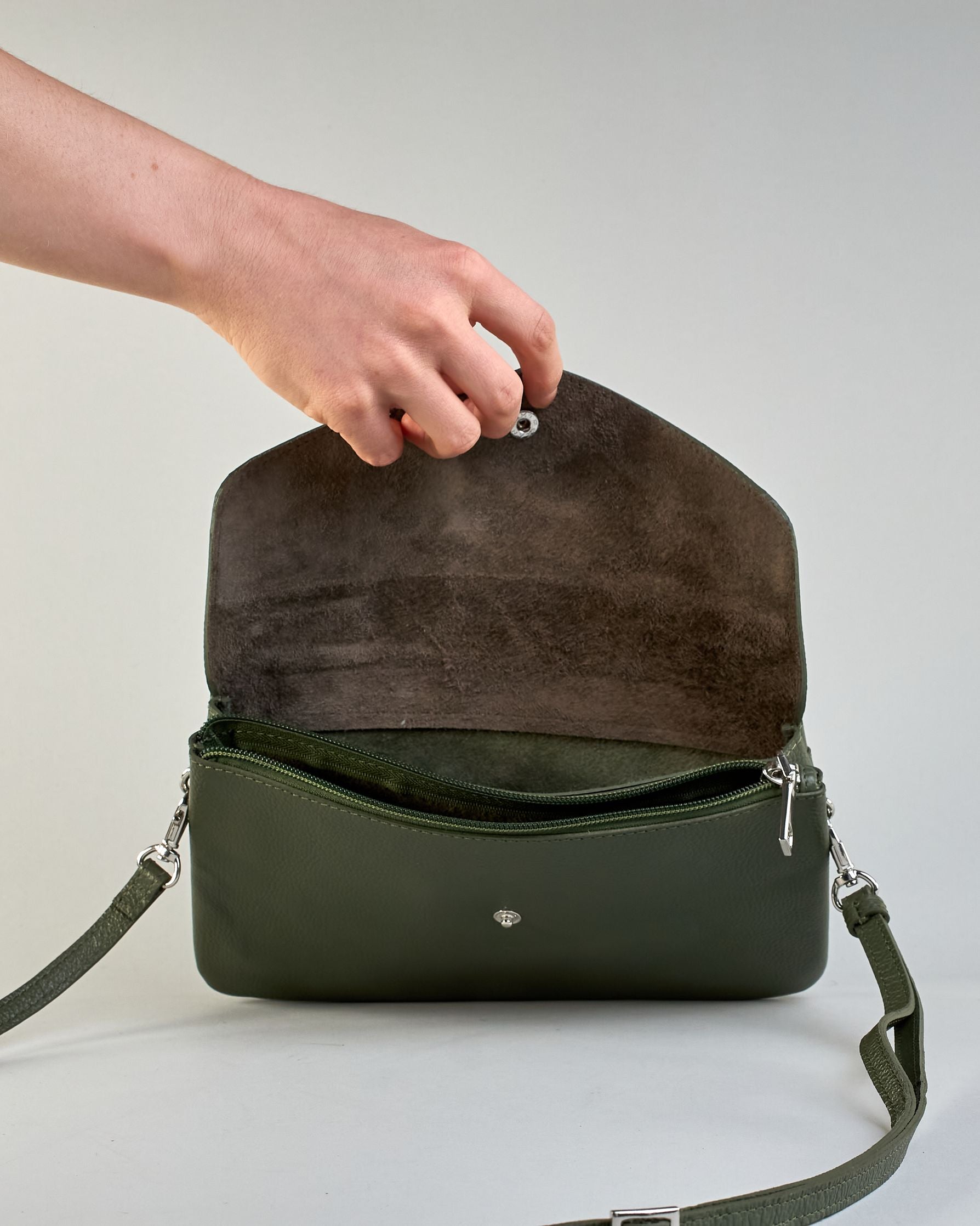 Einfärbige kleine Crossbody-Tasche aus genarbtem Rindleder mit Umschlaglasche und silbernem Druckknopf. Die Tasche enthält innen ein Zippfach, ein offenes Fach sowie ein schmales Zwischenfach. Auf der Rückseite ist eine Logoprägung "Herzilein-Wien" #40