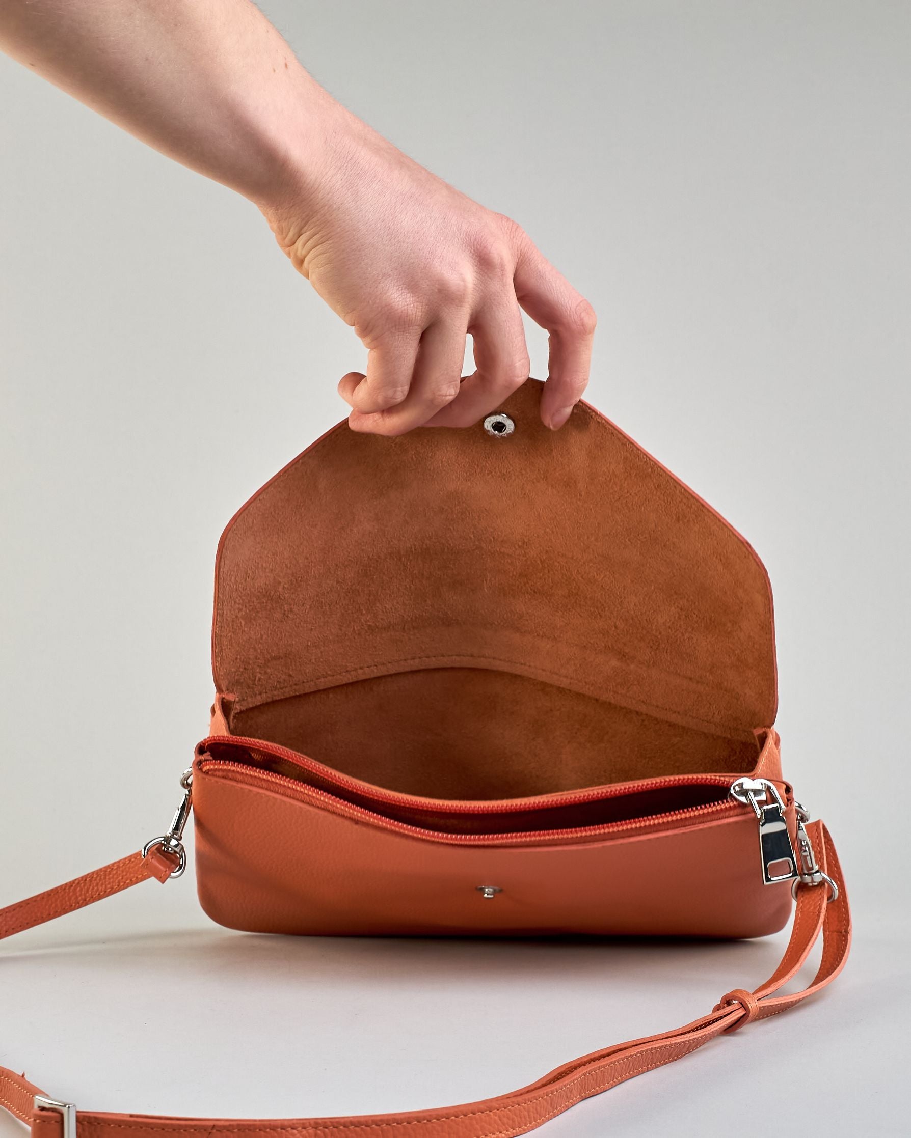 Einfärbige kleine Crossbody-Tasche aus genarbtem Rindleder mit Umschlaglasche und silbernem Druckknopf. Die Tasche enthält innen ein Zippfach, ein offenes Fach sowie ein schmales Zwischenfach. Auf der Rückseite ist eine Logoprägung "Herzilein-Wien" #52