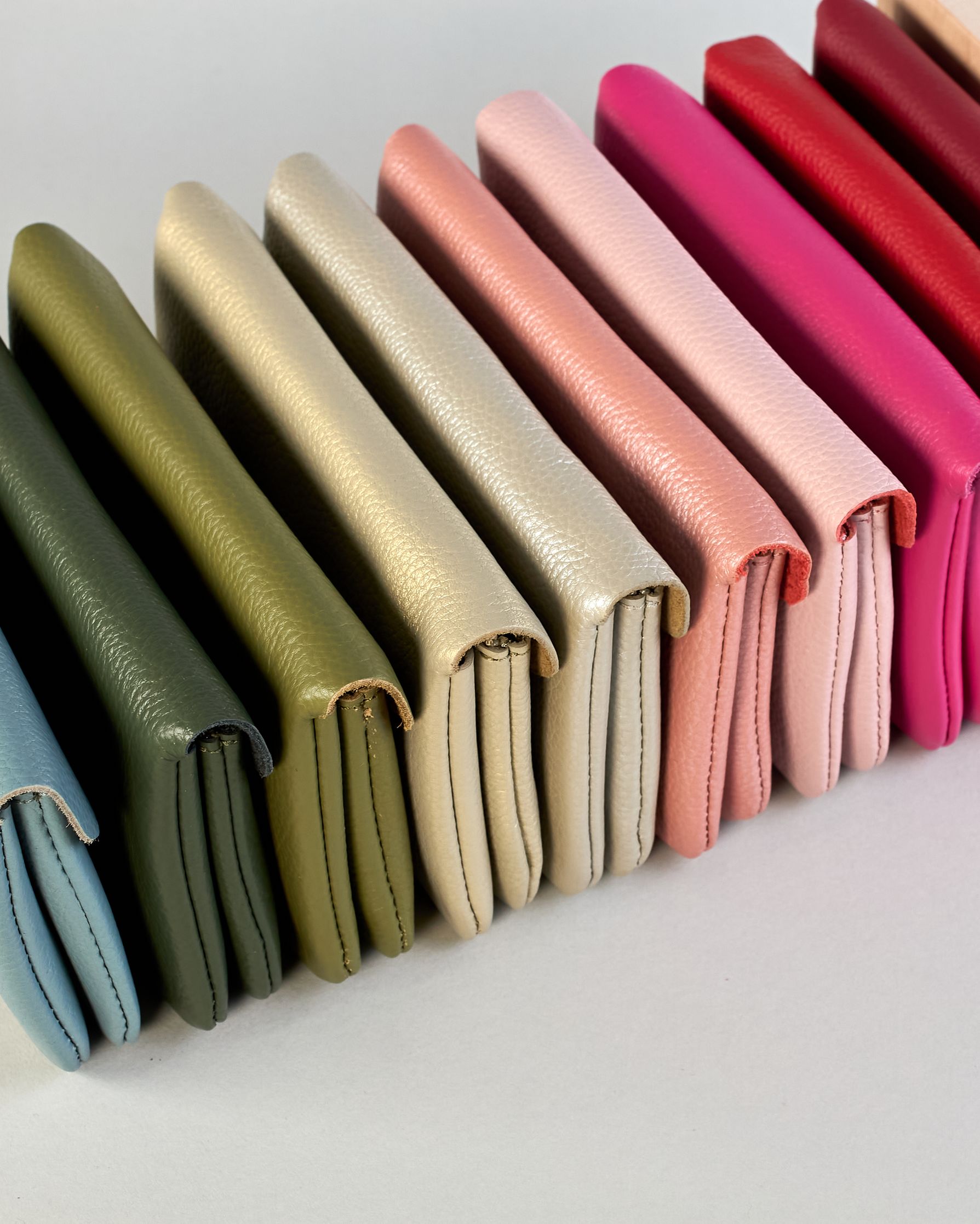 Geldbörse aus genarbtem Rindleder mit Umschlaglasche und silbernem Druckknopf. Die Geldbörse enthält innen ein Zippfach, ein offenes Fach sowie ein schmales Zwischenfach. Auf der Rückseite ist eine Logoprägung "Herzilein-Wien"