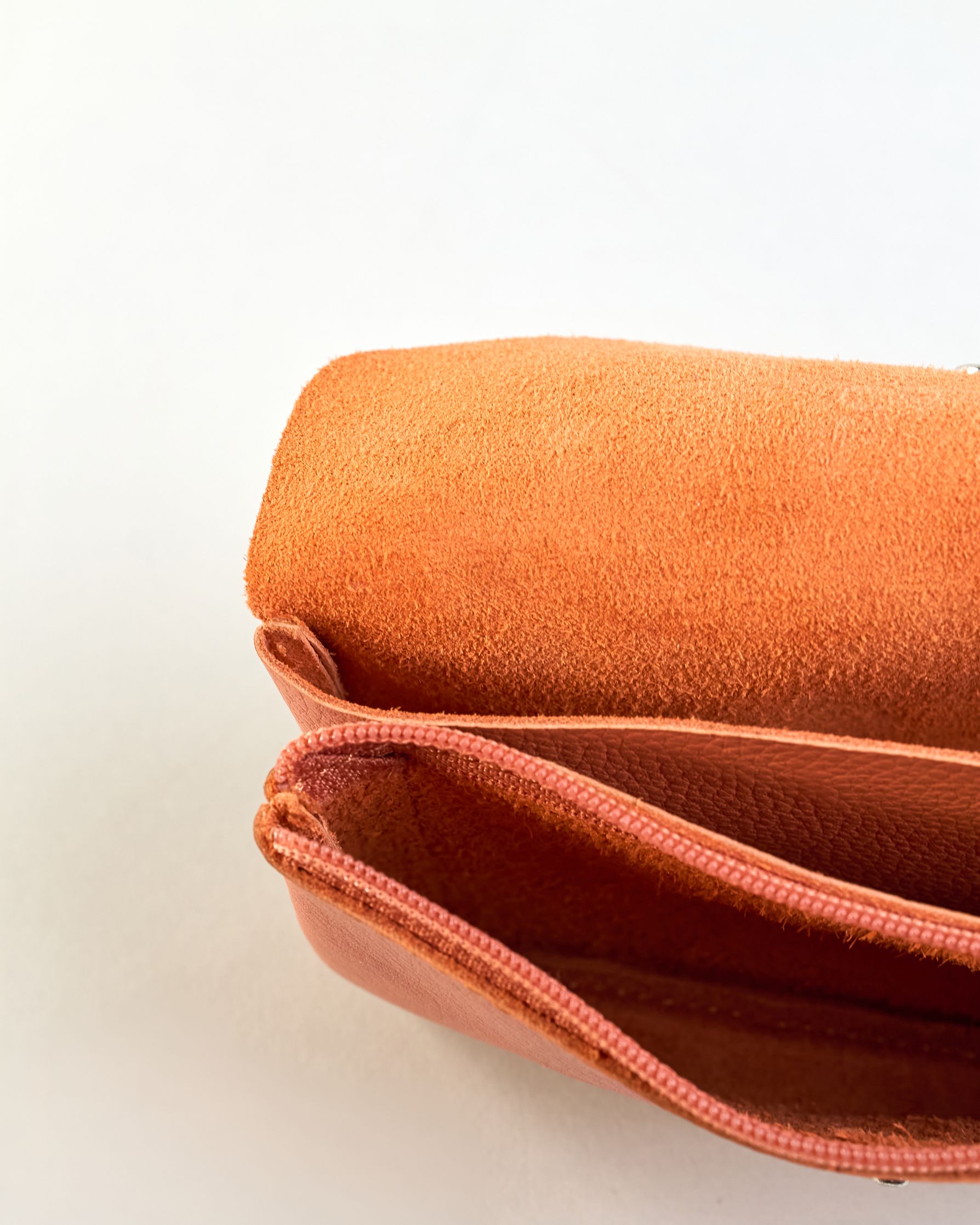 Geldbörse aus genarbtem Rindleder mit Umschlaglasche und silbernem Druckknopf. Die Geldbörse enthält innen ein Zippfach, ein offenes Fach sowie ein schmales Zwischenfach. Auf der Rückseite ist eine Logoprägung "Herzilein-Wien"