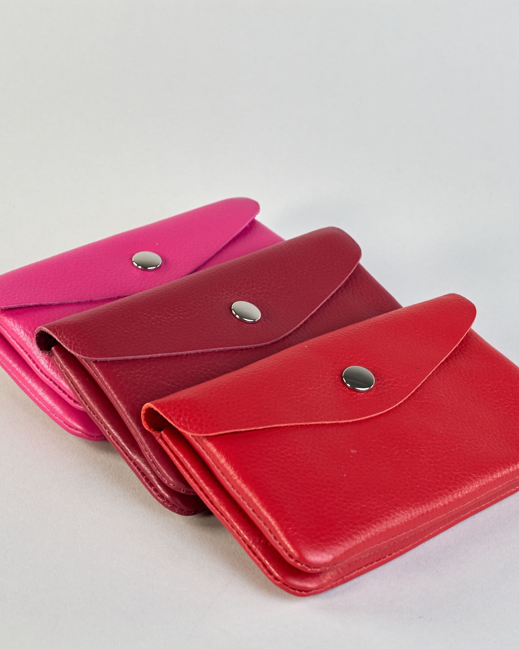 Geldbörse aus genarbtem Rindleder mit Umschlaglasche und silbernem Druckknopf. Die Geldbörse enthält innen ein Zippfach, ein offenes Fach sowie ein schmales Zwischenfach. Auf der Rückseite ist eine Logoprägung "Herzilein-Wien"