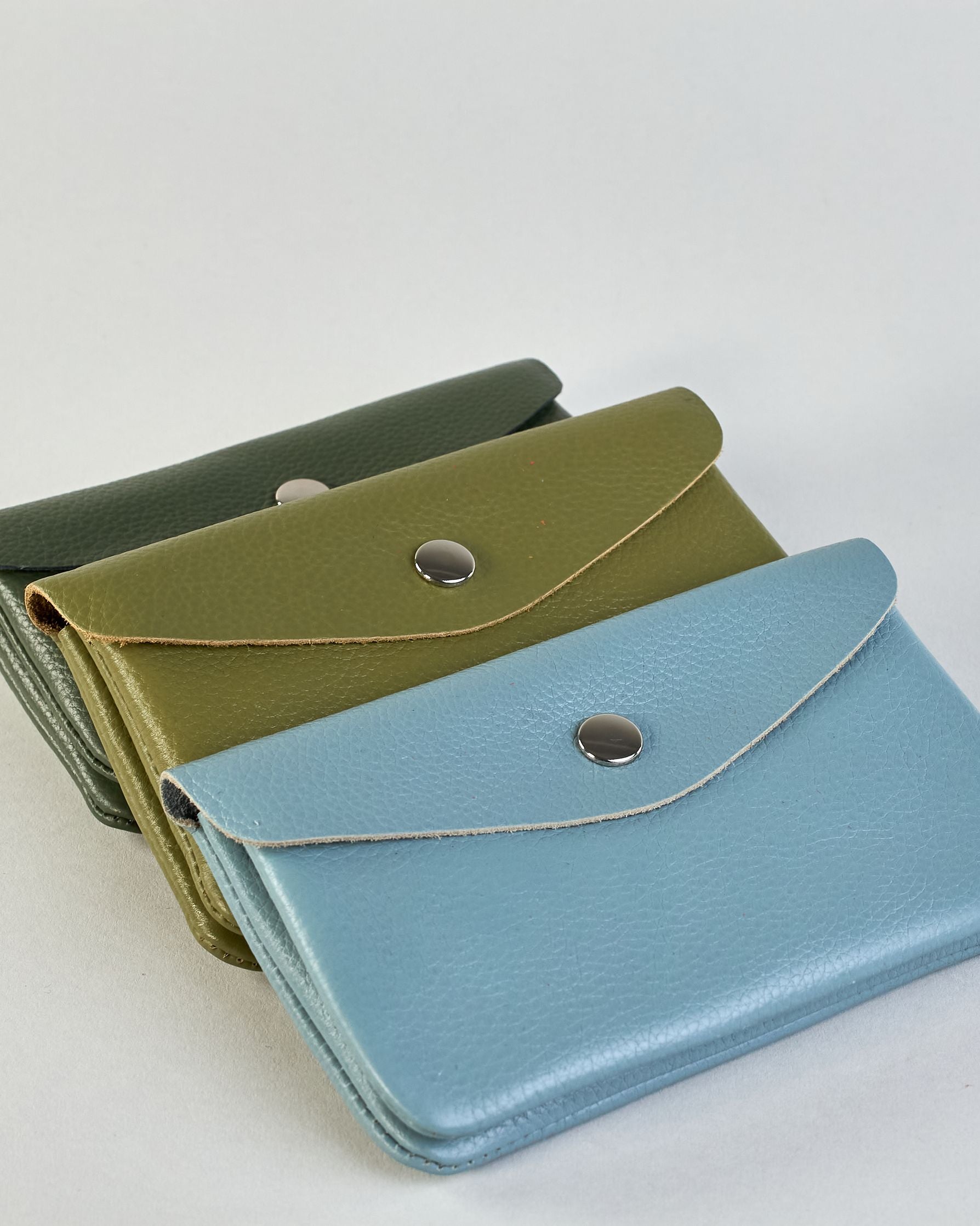 Geldbörse aus genarbtem Rindleder mit Umschlaglasche und silbernem Druckknopf. Die Geldbörse enthält innen ein Zippfach, ein offenes Fach sowie ein schmales Zwischenfach. Auf der Rückseite ist eine Logoprägung "Herzilein-Wien"