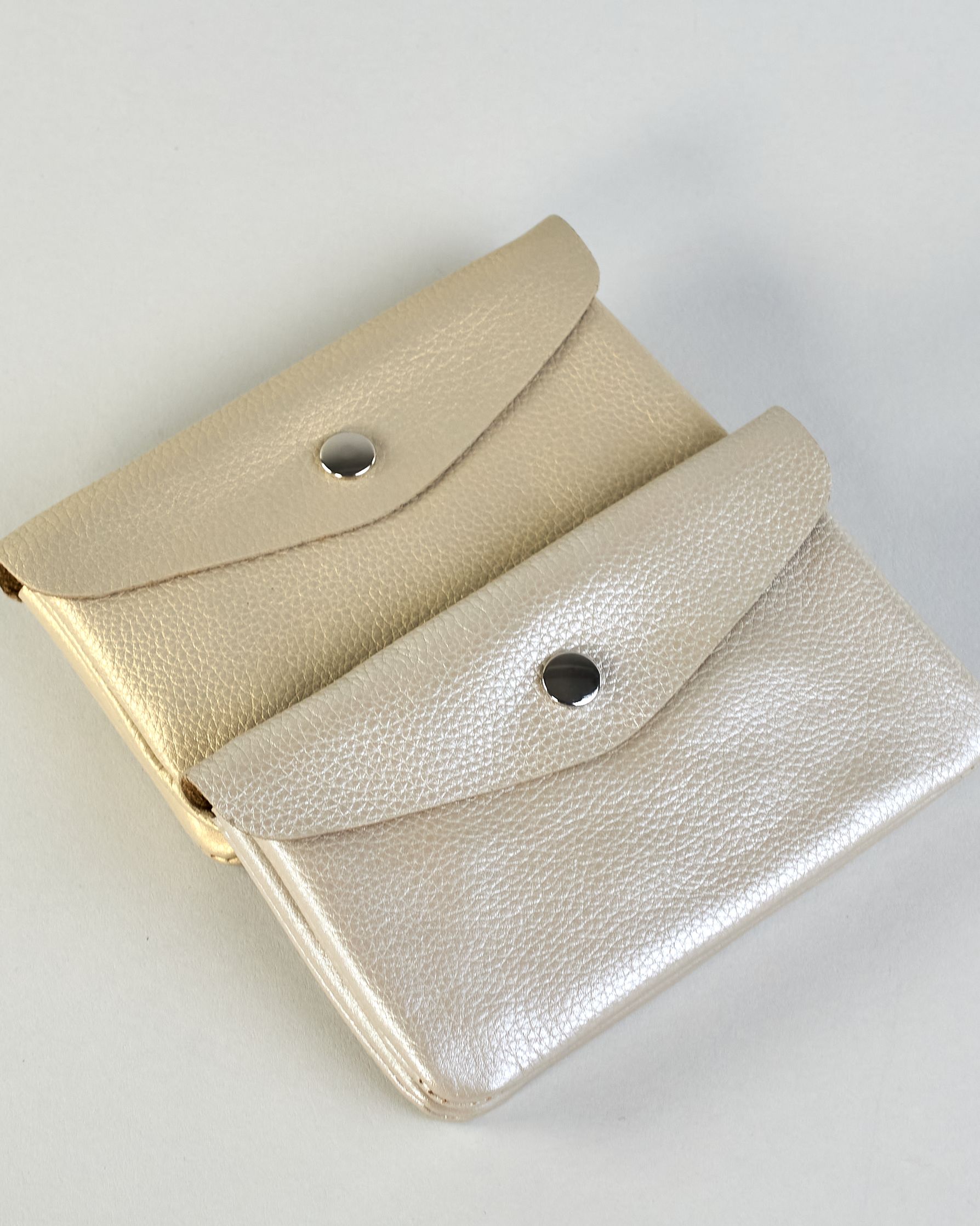 Geldbörse aus genarbtem Rindleder mit Umschlaglasche und silbernem Druckknopf. Die Geldbörse enthält innen ein Zippfach, ein offenes Fach sowie ein schmales Zwischenfach. Auf der Rückseite ist eine Logoprägung "Herzilein-Wien"