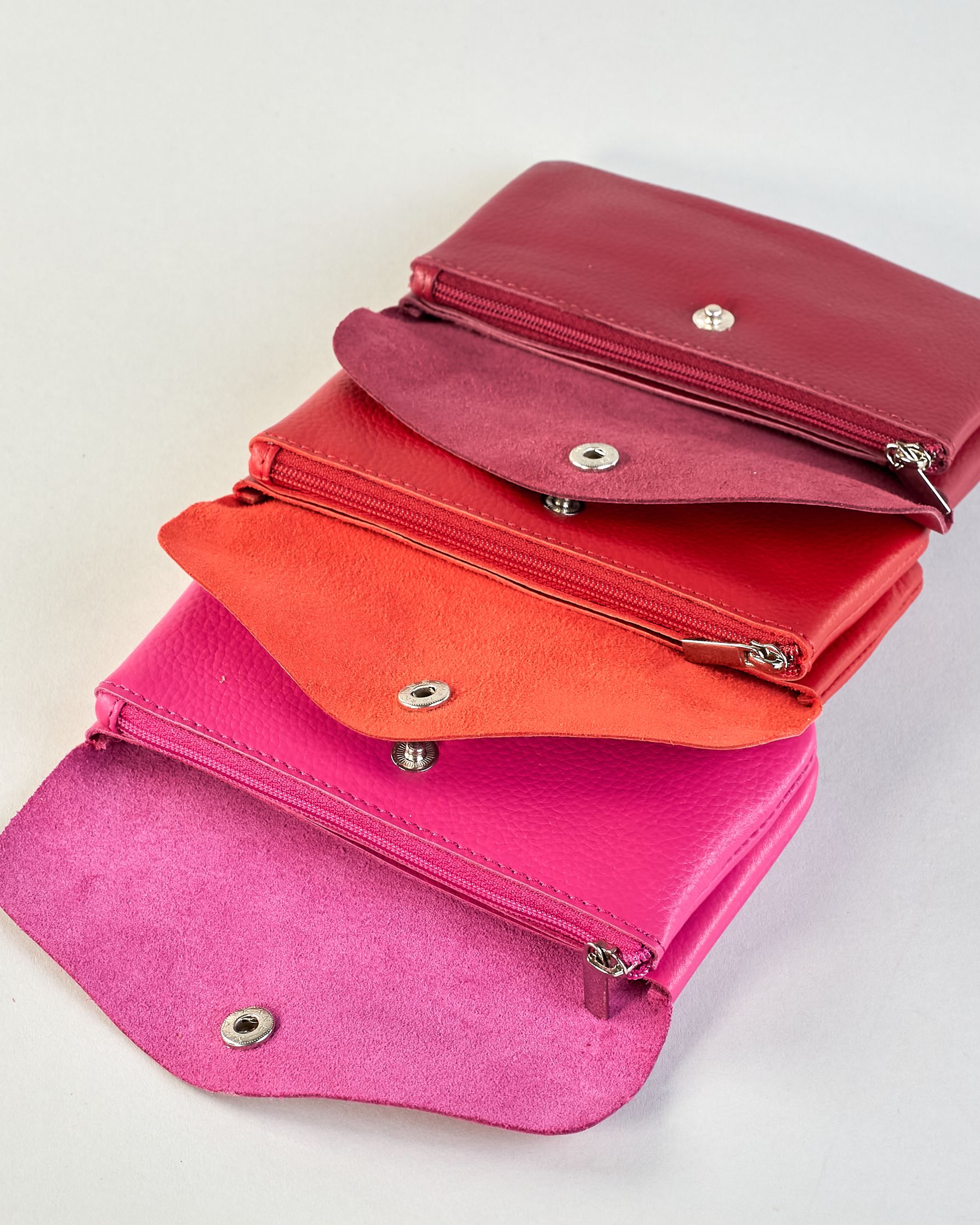 Geldbörse aus genarbtem Rindleder mit Umschlaglasche und silbernem Druckknopf. Die Geldbörse enthält innen ein Zippfach, ein offenes Fach sowie ein schmales Zwischenfach. Auf der Rückseite ist eine Logoprägung "Herzilein-Wien"