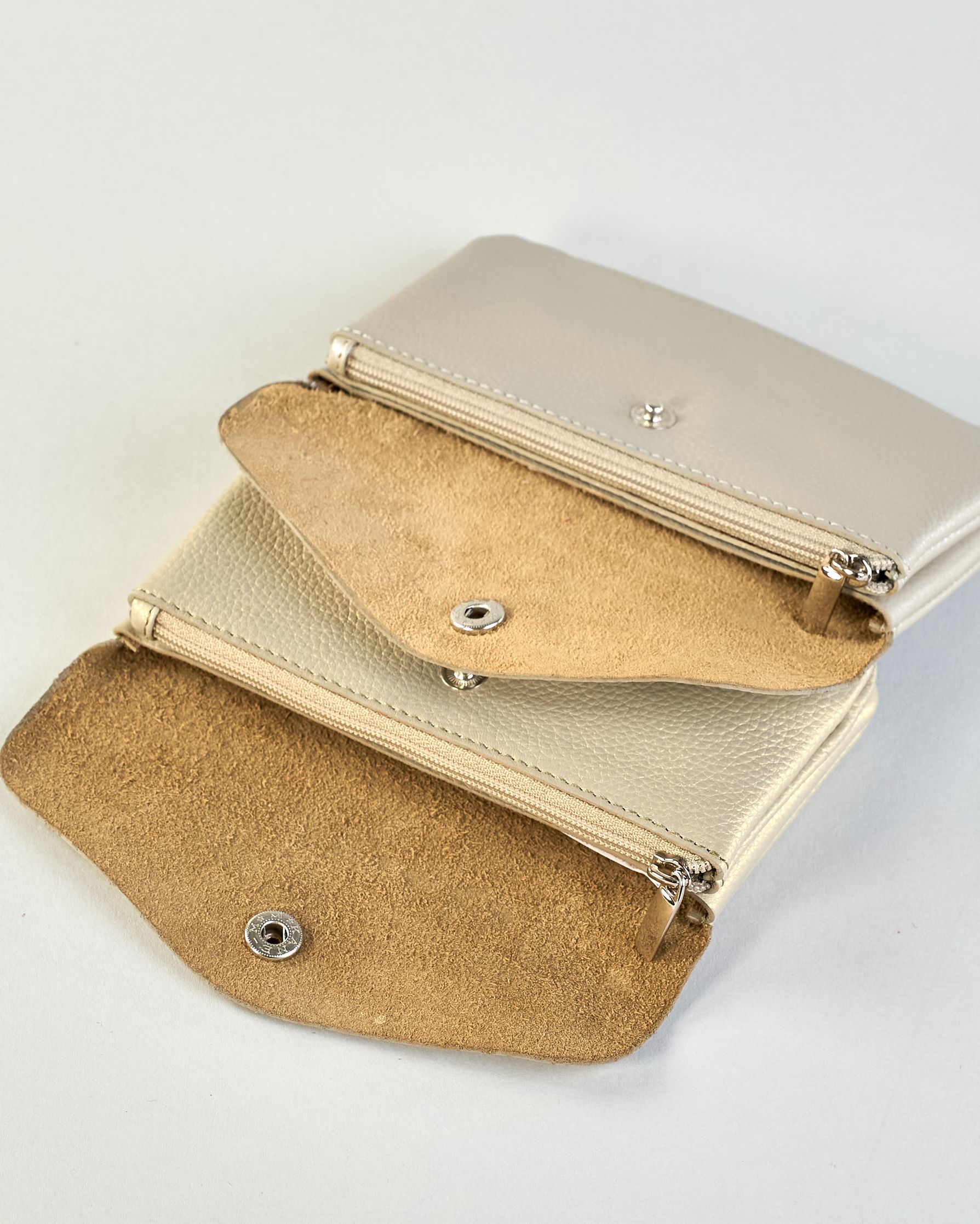 Geldbörse aus genarbtem Rindleder mit Umschlaglasche und silbernem Druckknopf. Die Geldbörse enthält innen ein Zippfach, ein offenes Fach sowie ein schmales Zwischenfach. Auf der Rückseite ist eine Logoprägung "Herzilein-Wien"