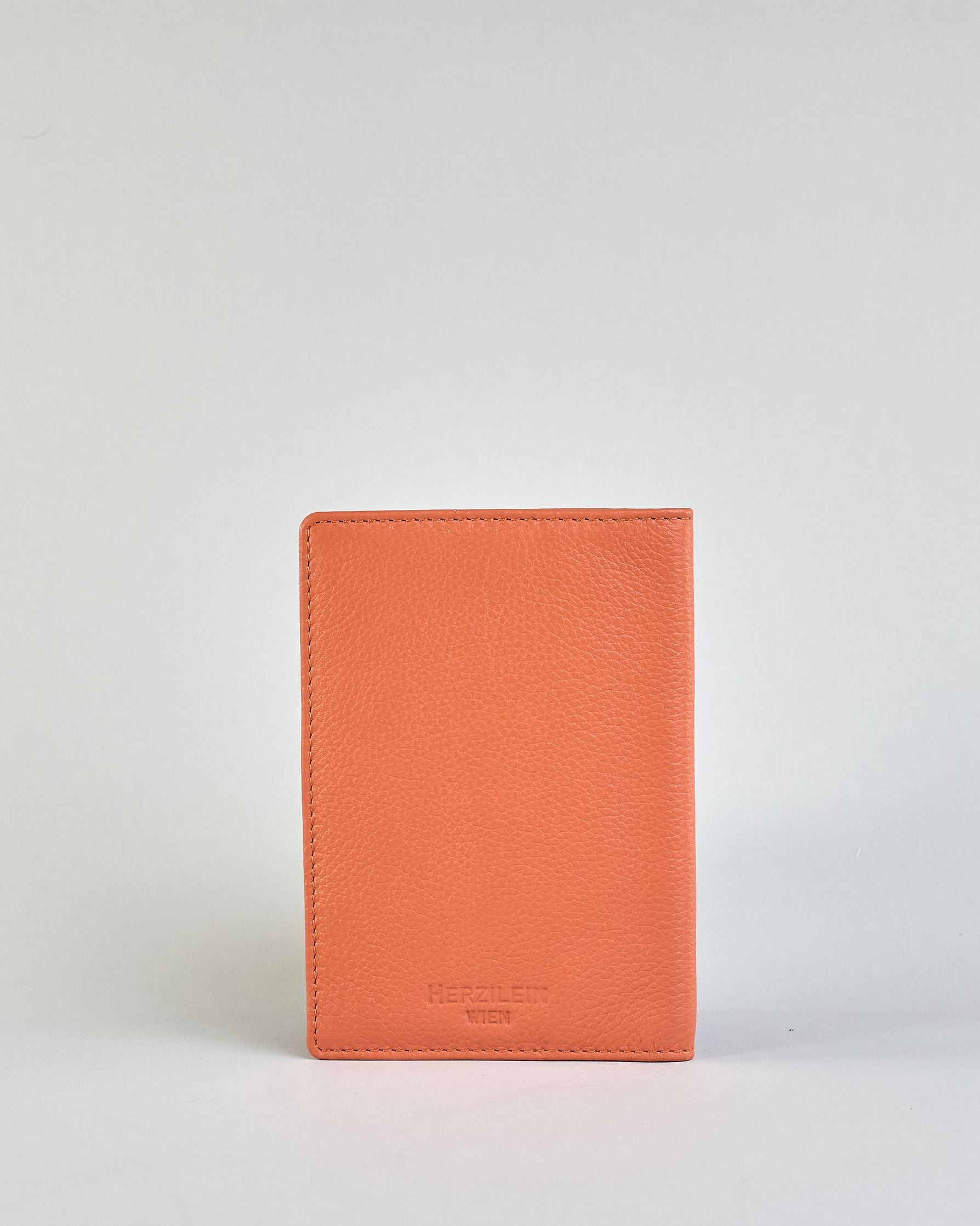 Einfärbige Reisepasshülle aus Leder, innen sind zwei Kartenfächer und ein Schlitz für den Reisepass. Auf der Rückseite ist die Logo Prägung dezent "Herzilein-Wien"