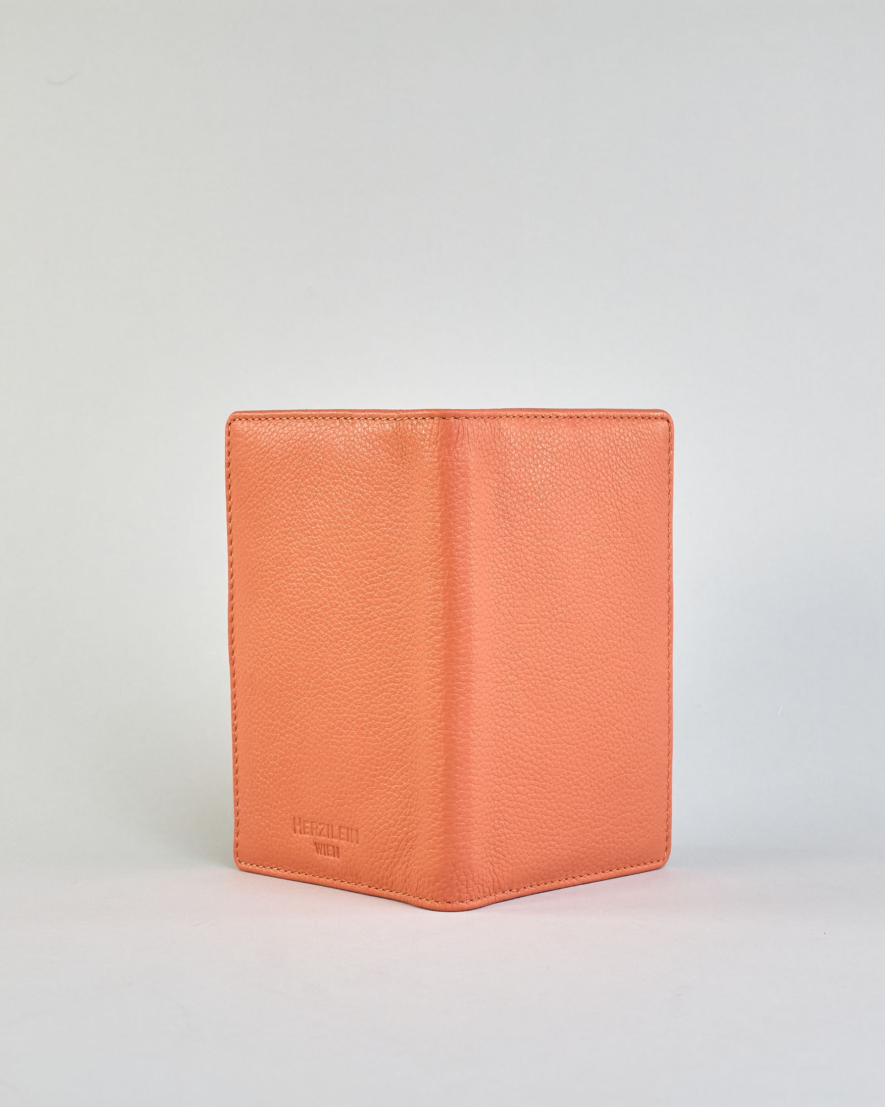 Einfärbige Reisepasshülle aus Leder, innen sind zwei Kartenfächer und ein Schlitz für den Reisepass. Auf der Rückseite ist die Logo Prägung dezent "Herzilein-Wien"