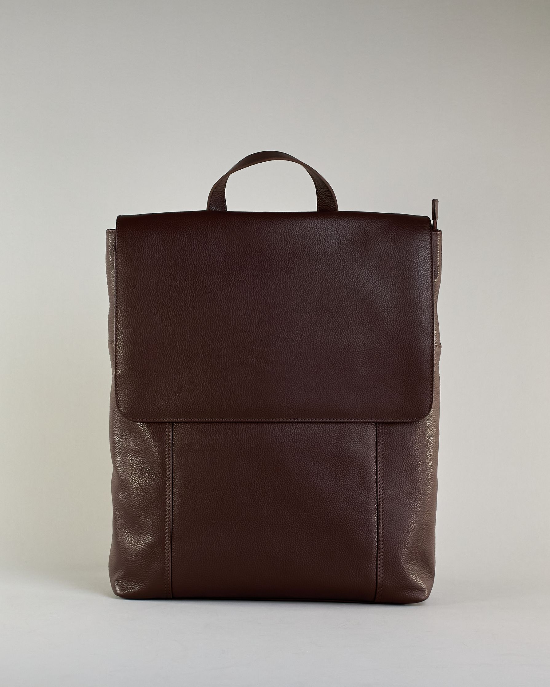 Brauner Rucksack aus Rindleder mit großer Überschlagklappe, verstellbaren Schulterriemen und mehreren Innen- und Außenfächern. Er ist simpel gestaltet und hat nur ein kleines Logo "Herzilein-Wien" unter der Lasche. #1