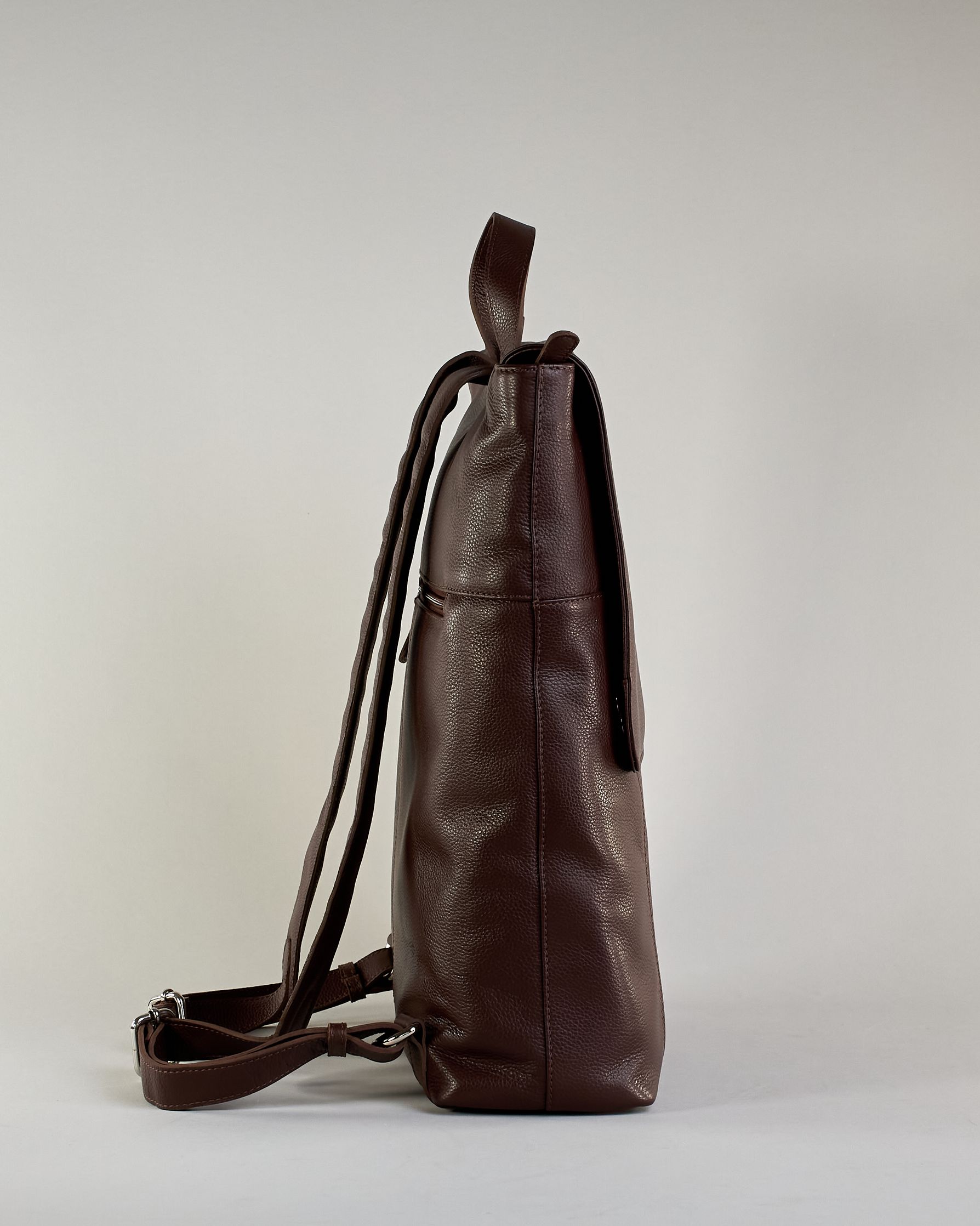 Brauner Rucksack aus Rindleder mit großer Überschlagklappe, verstellbaren Schulterriemen und mehreren Innen- und Außenfächern. Er ist simpel gestaltet und hat nur ein kleines Logo "Herzilein-Wien" unter der Lasche. #6