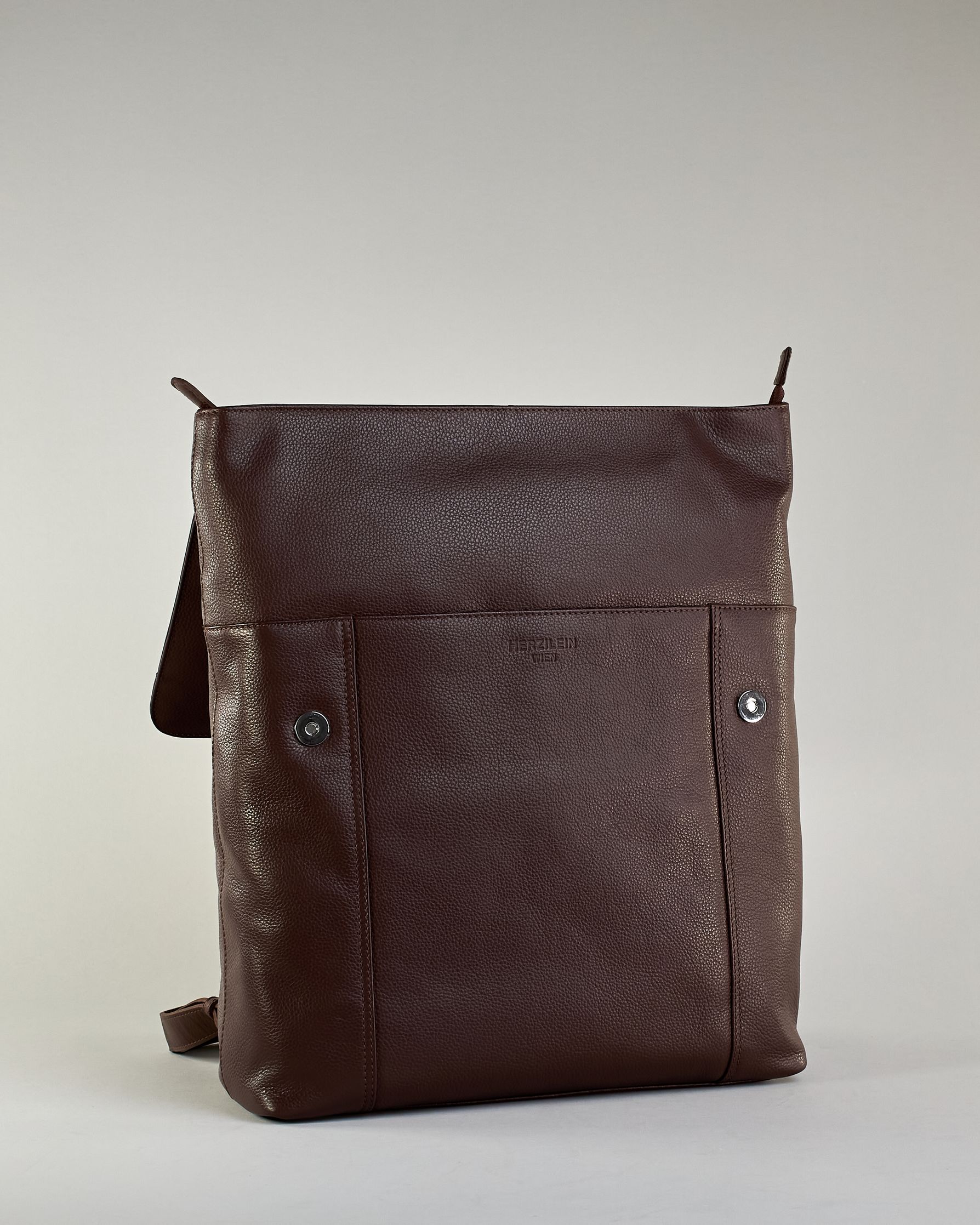 Brauner Rucksack aus Rindleder mit großer Überschlagklappe, verstellbaren Schulterriemen und mehreren Innen- und Außenfächern. Er ist simpel gestaltet und hat nur ein kleines Logo "Herzilein-Wien" unter der Lasche. #7